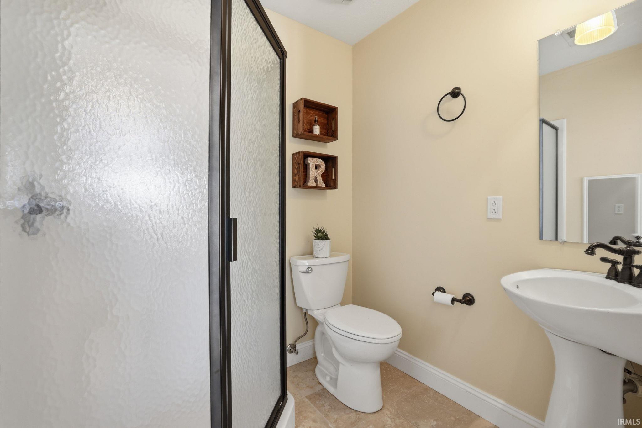 Bathroom with a frosted-glass shower, white toilet, pedestal sink, and rustic wooden shelves.