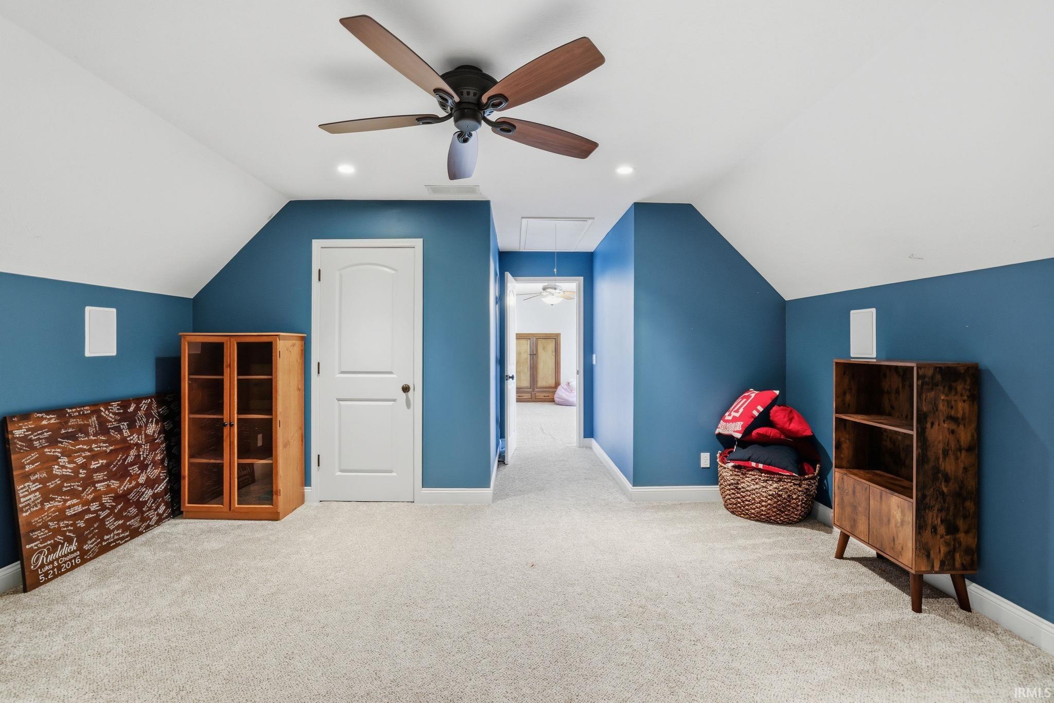 Carpeted bonus room with blue walls, a sloped ceiling, and a wood-bladed ceiling fan.