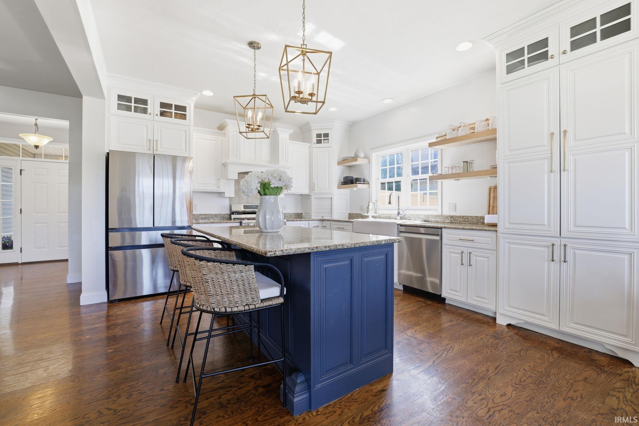 Kitchen with a blue island, woven stools, white cabinetry, stainless appliances, and dark hardwood floors.