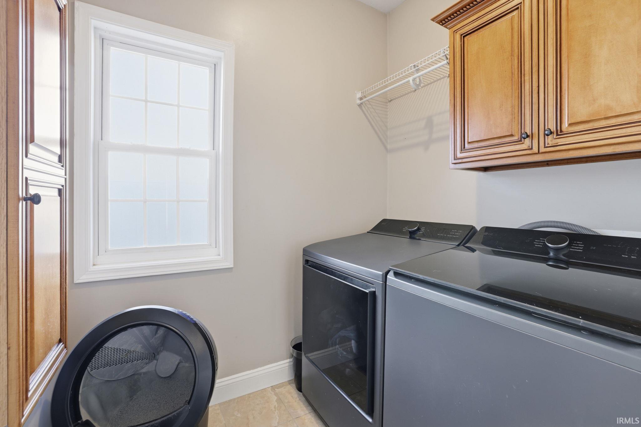 Laundry room with front-loading washer and dryer beneath wood cabinets.