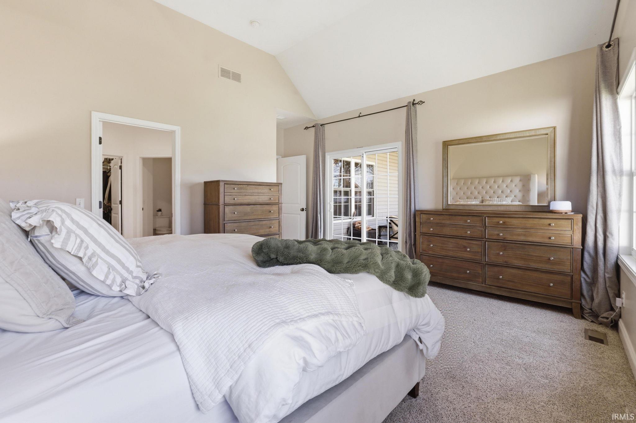 Furnished bedroom with a vaulted ceiling, wooden dressers, and sliding glass doors to a patio.