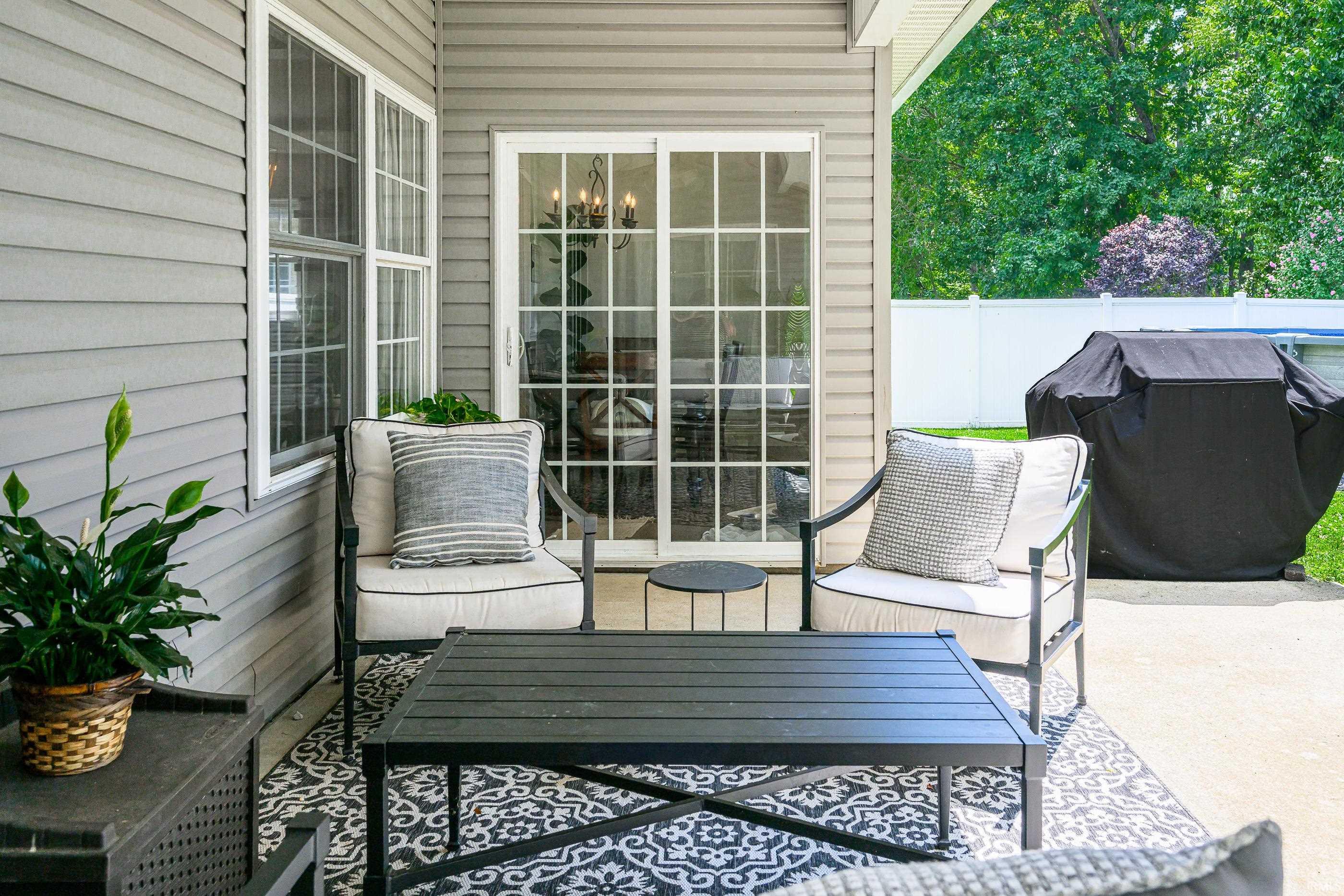 Furnished patio with cushioned chairs, a black coffee table, and a covered grill beside the home.