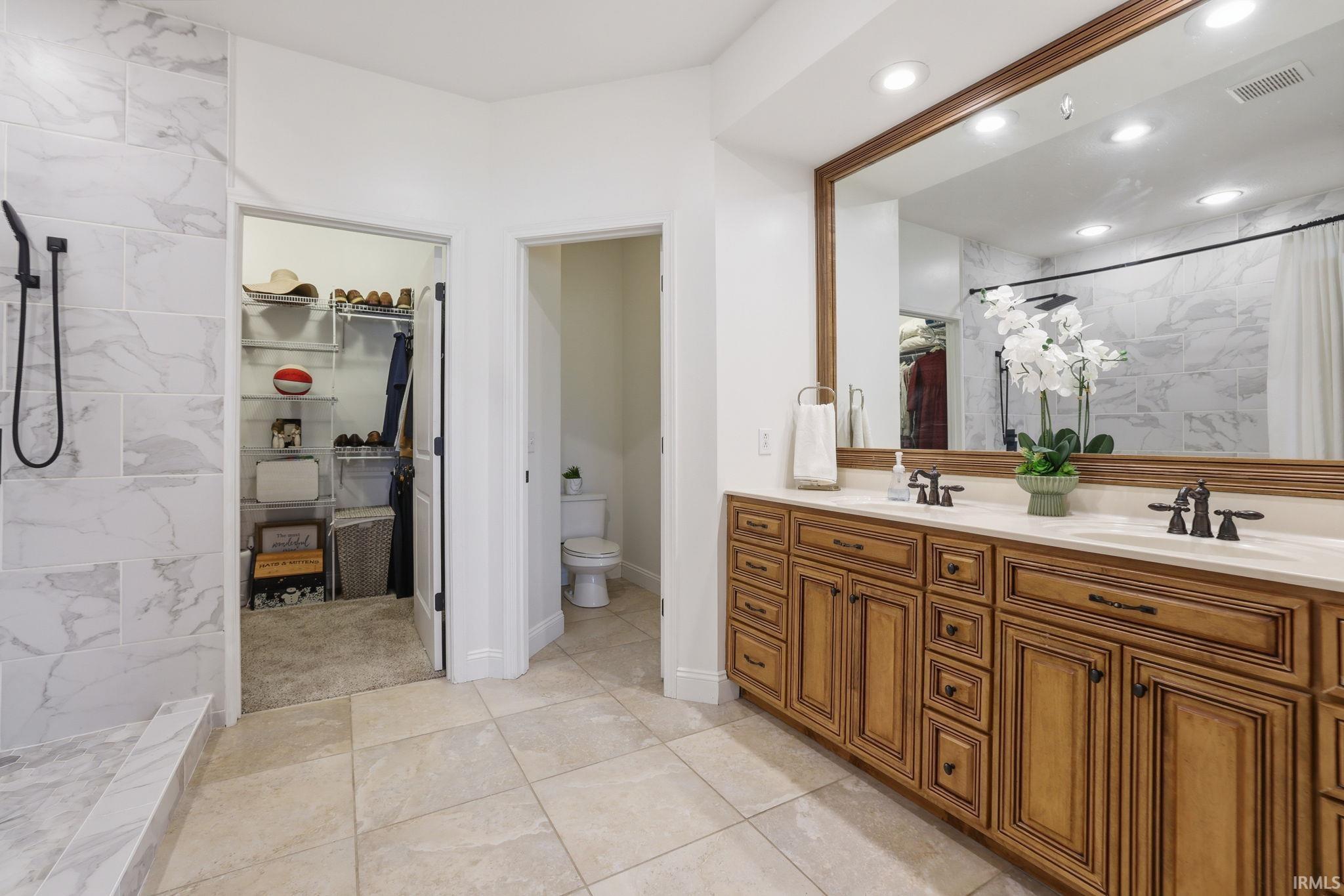 Primary bathroom with a long wood double vanity, marble-look tile, and adjoining walk-in closet.