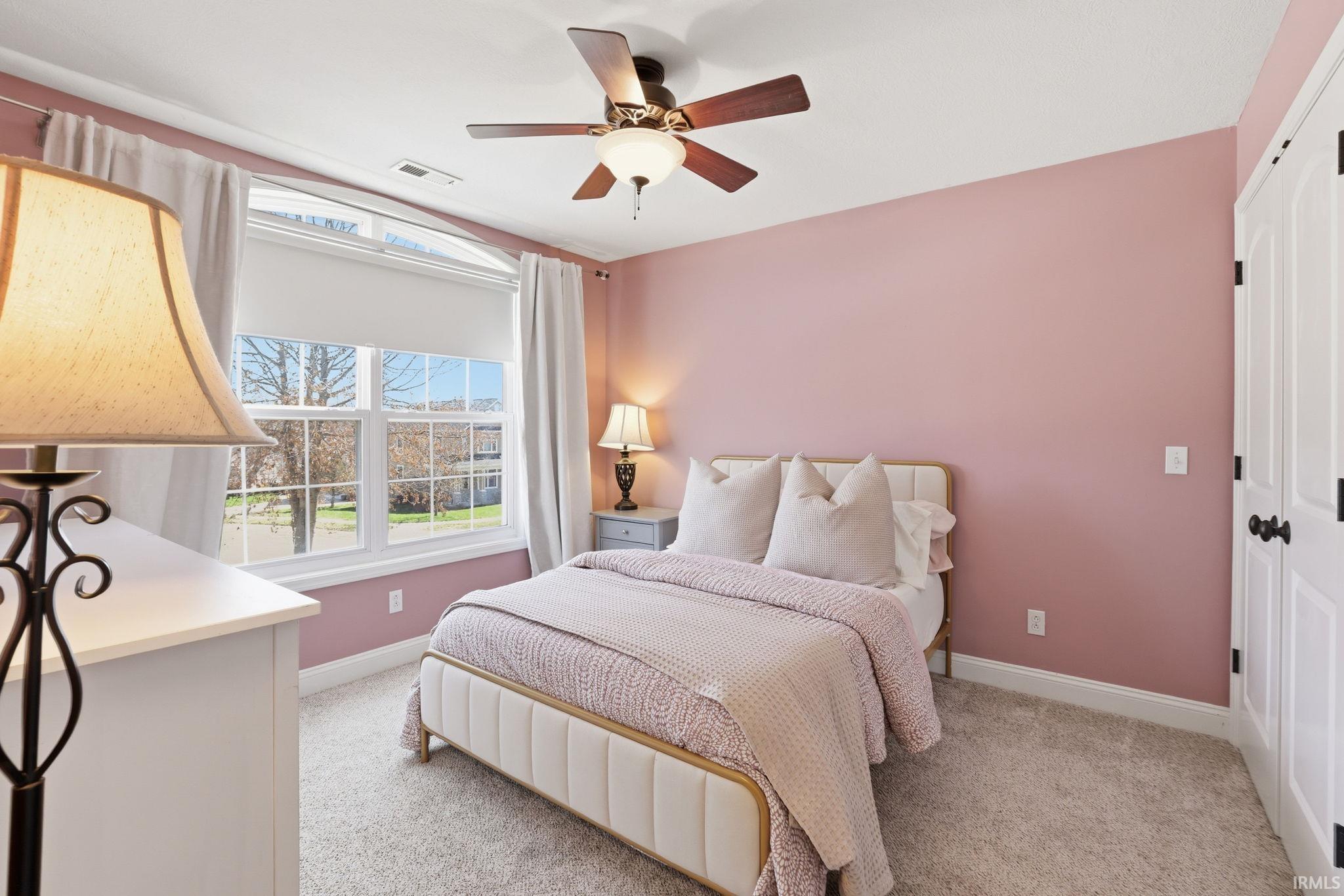 Bedroom with pink walls, a cream upholstered bed, and a large curtained window.