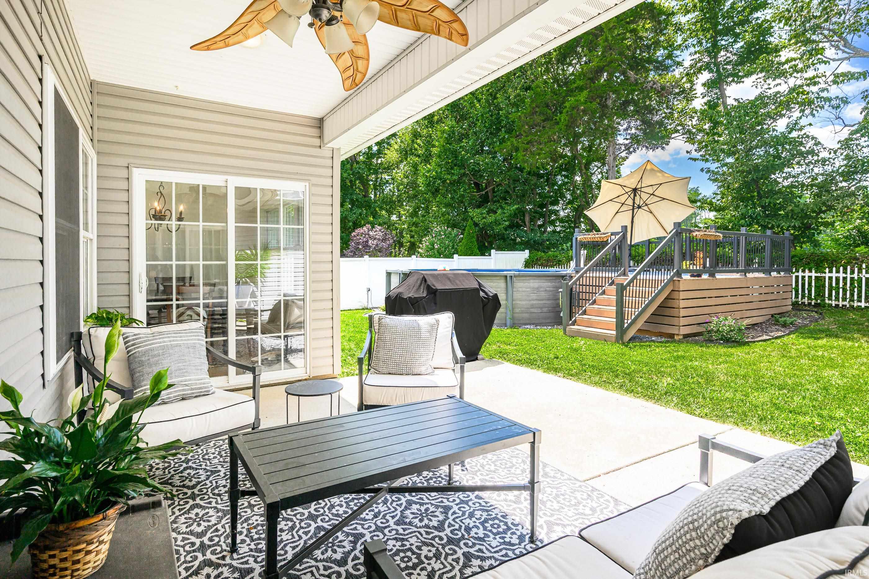 Covered patio with cushioned seating overlooks a fenced backyard, raised deck, and swimming pool.