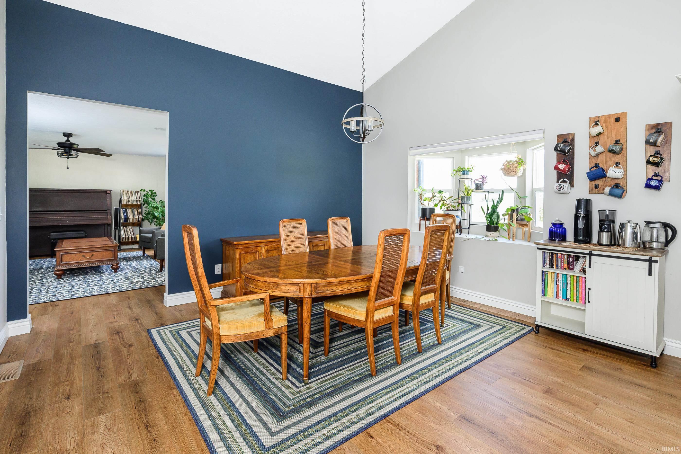 Dining room with a wooden table, cane-back chairs, striped rug, and blue accent wall.