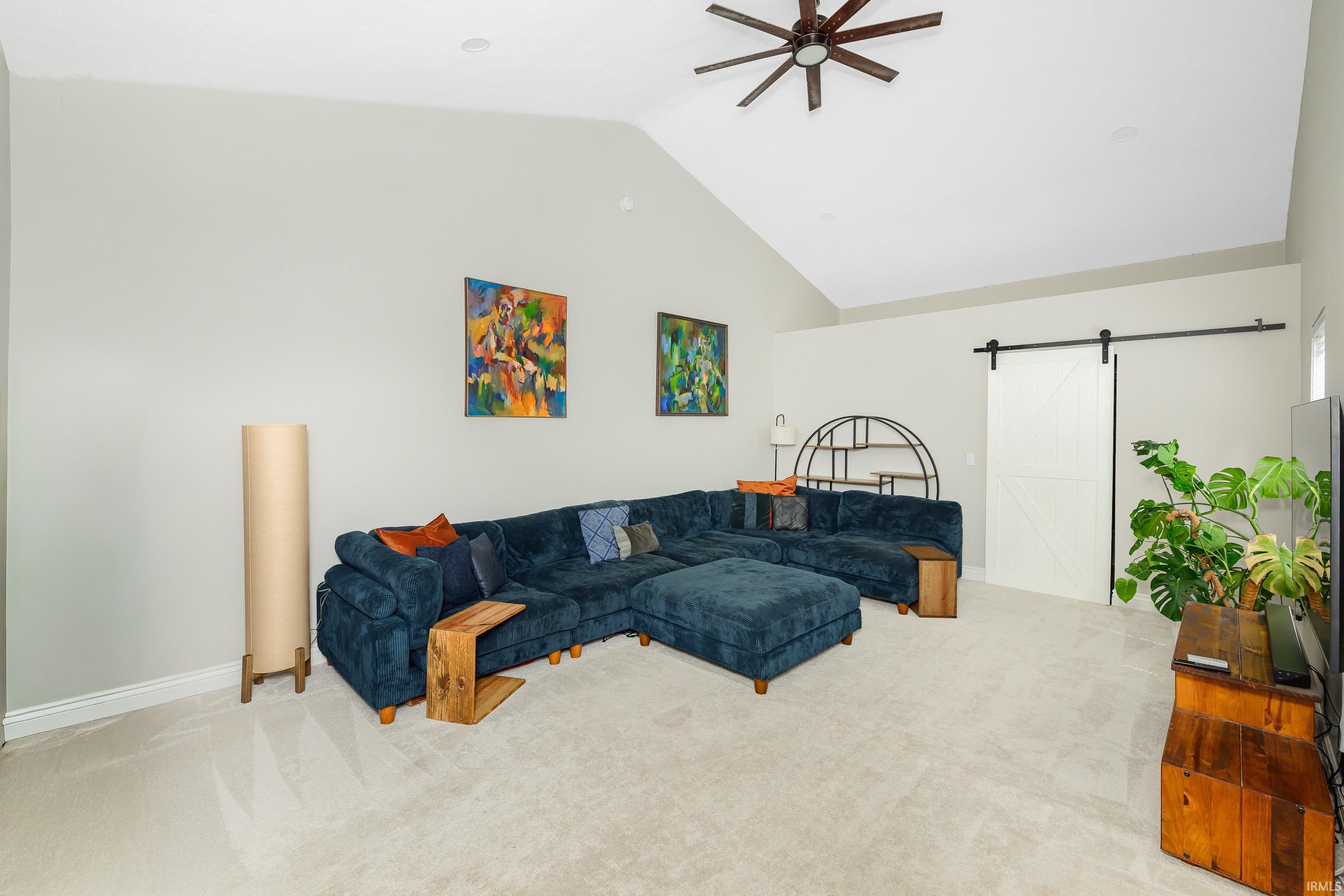 Living room with a dark blue sectional beneath a vaulted ceiling and white sliding barn door.