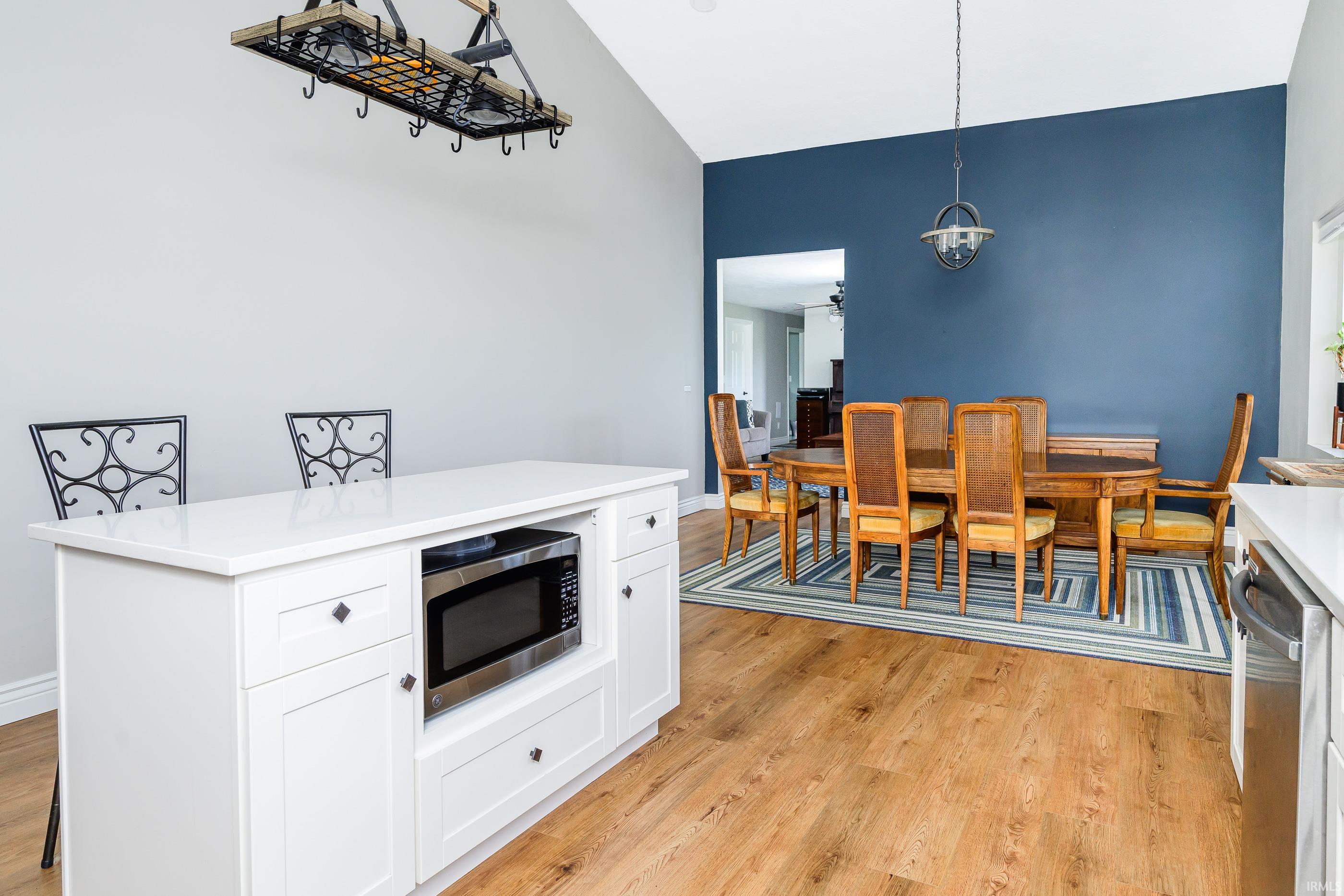 Kitchen and dining area with a white island, wooden table, blue accent wall, and hardwood floors.