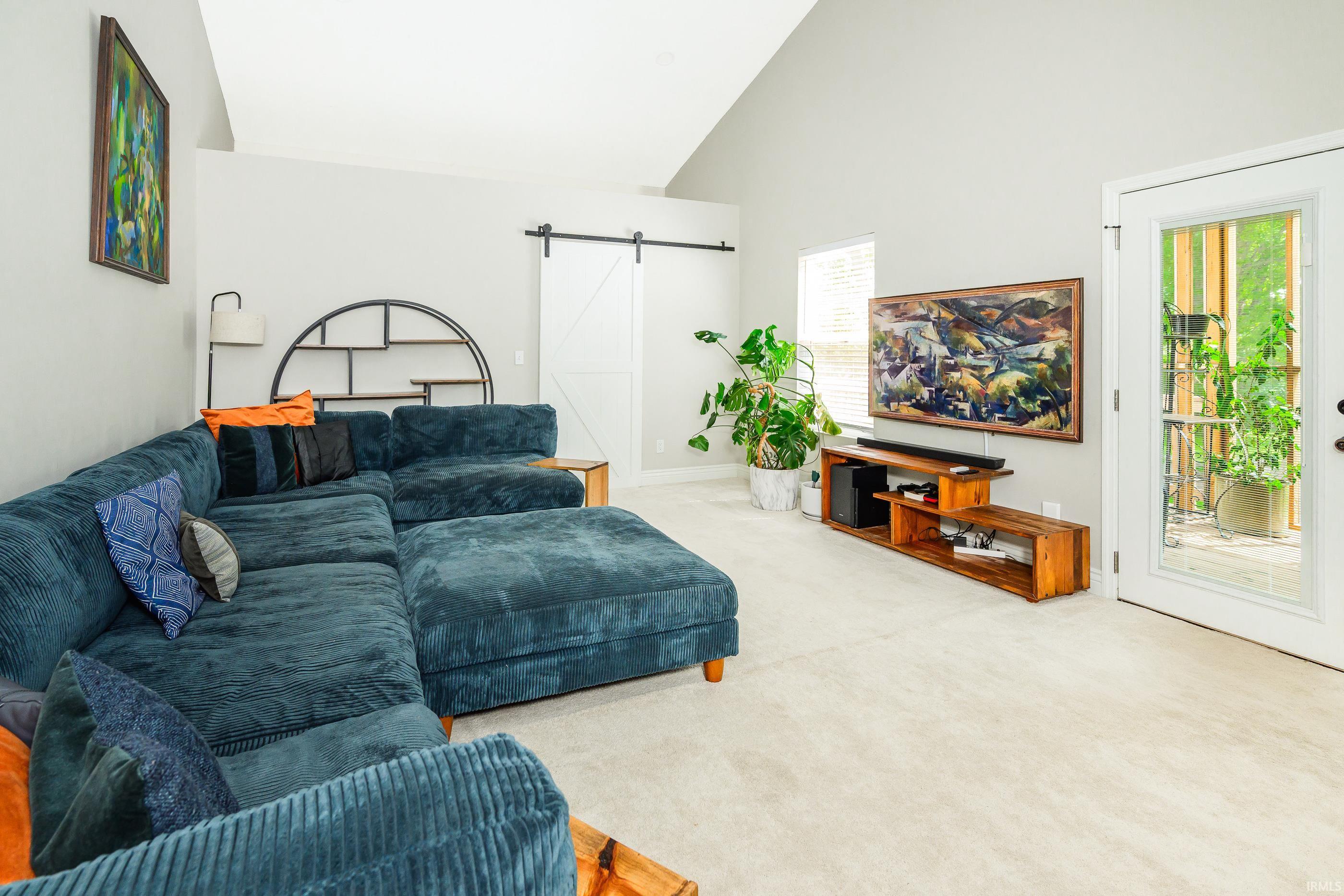 Living room with a deep-blue sectional, abstract artwork, and a glass-paneled door beside a greenery-filled porch.