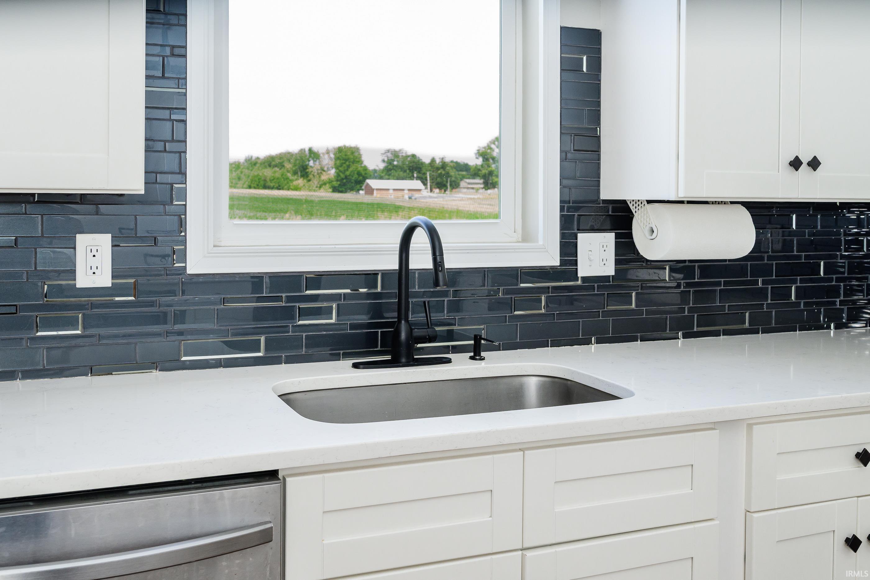 Kitchen sink with a black faucet, dark blue tile backsplash, and window overlooking a field.