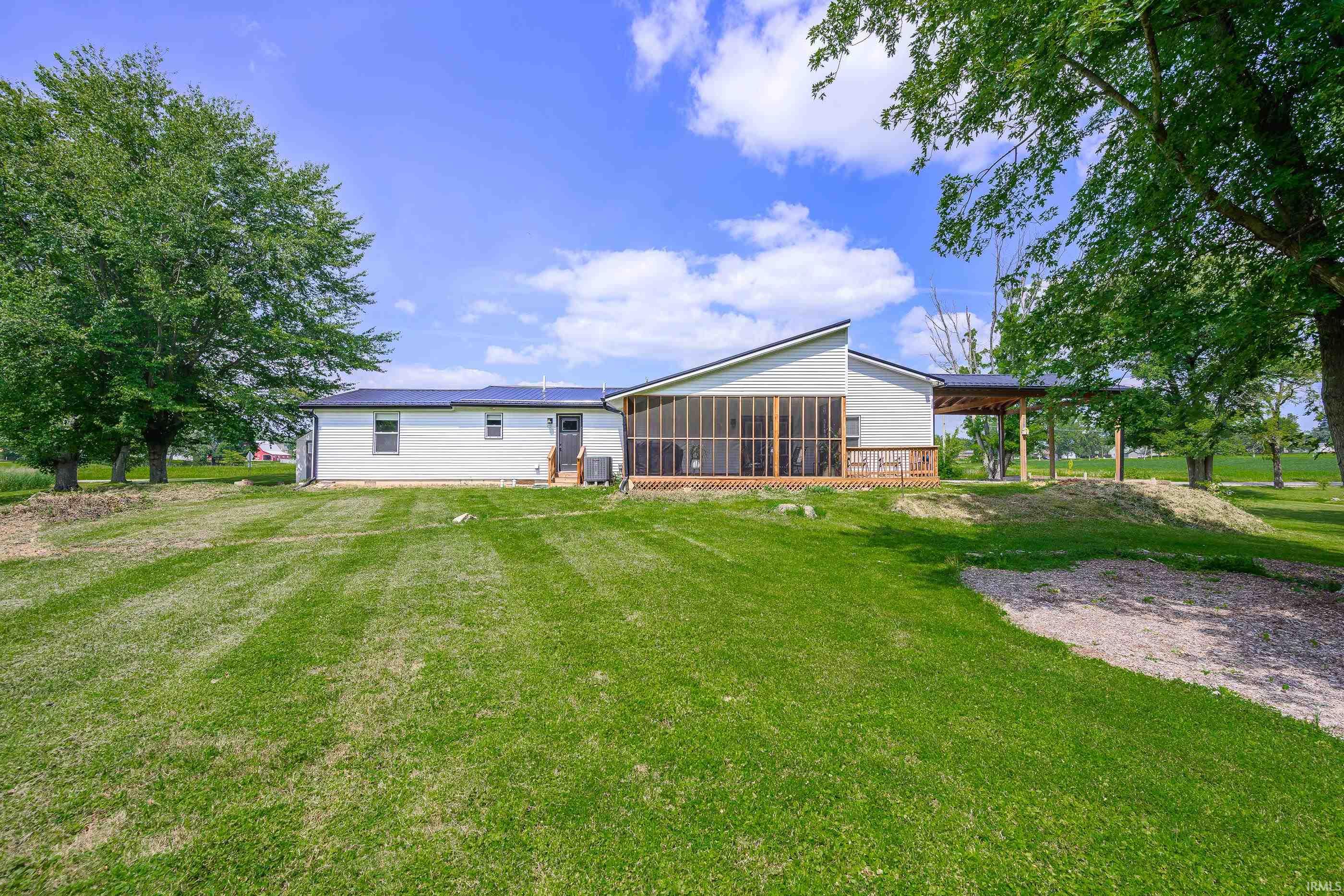 Rear of a white-sided home with a screened porch, covered patio, solar panels, and a broad lawn.