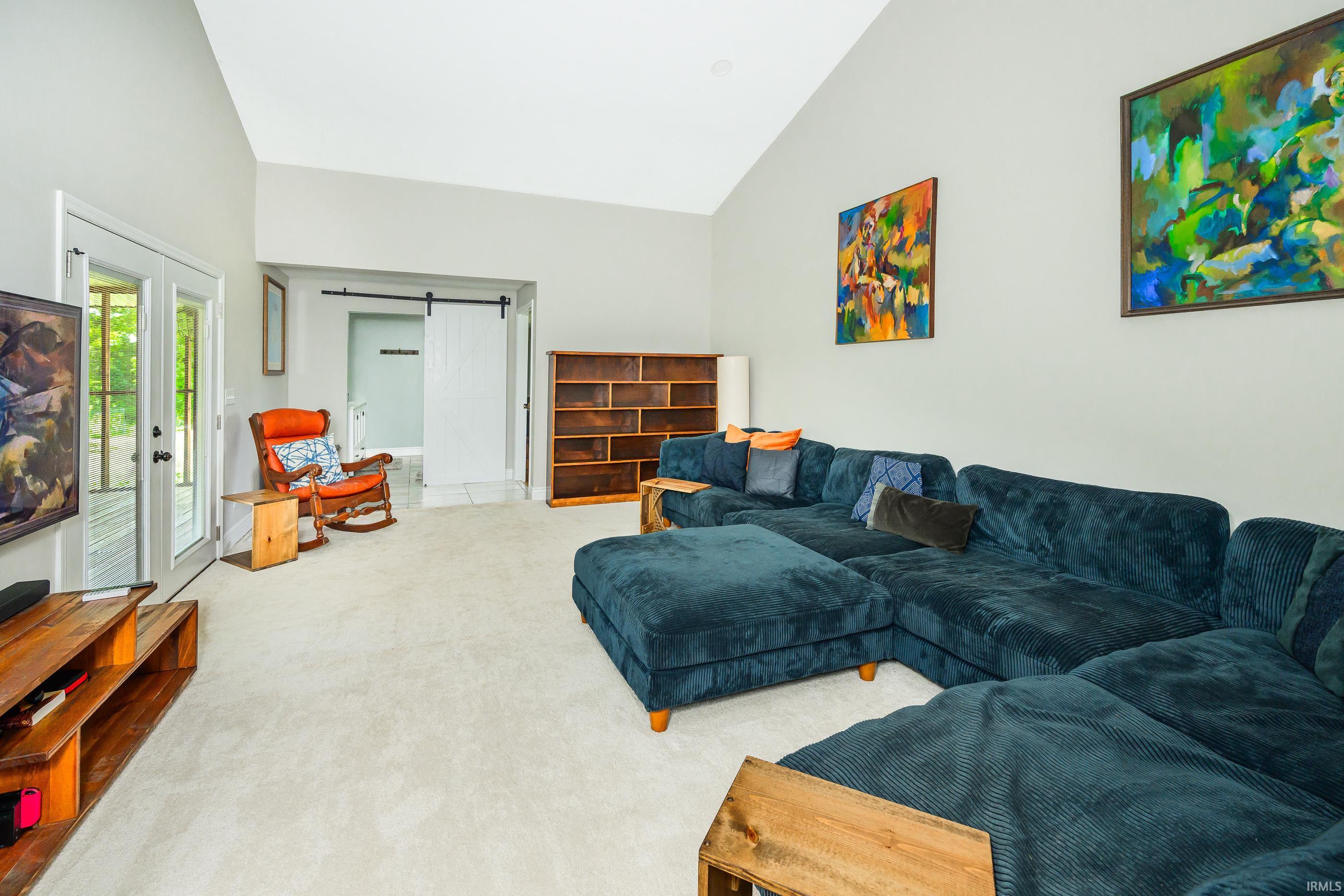 Living room with a dark teal sectional, colorful wall art, and a white sliding barn door.
