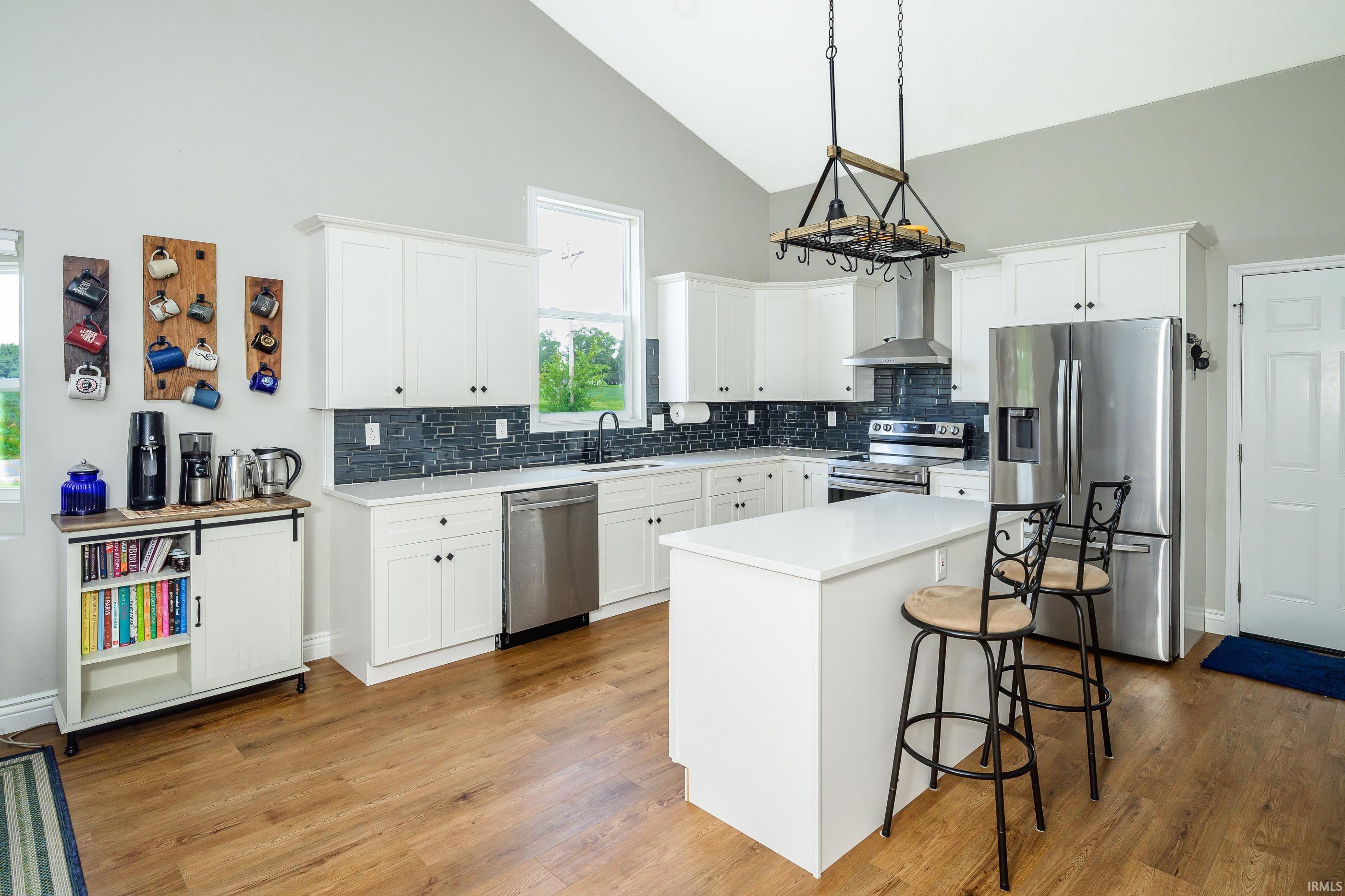 Bright kitchen with white cabinetry, dark tile backsplash, stainless steel appliances, and a large island with bar stools.