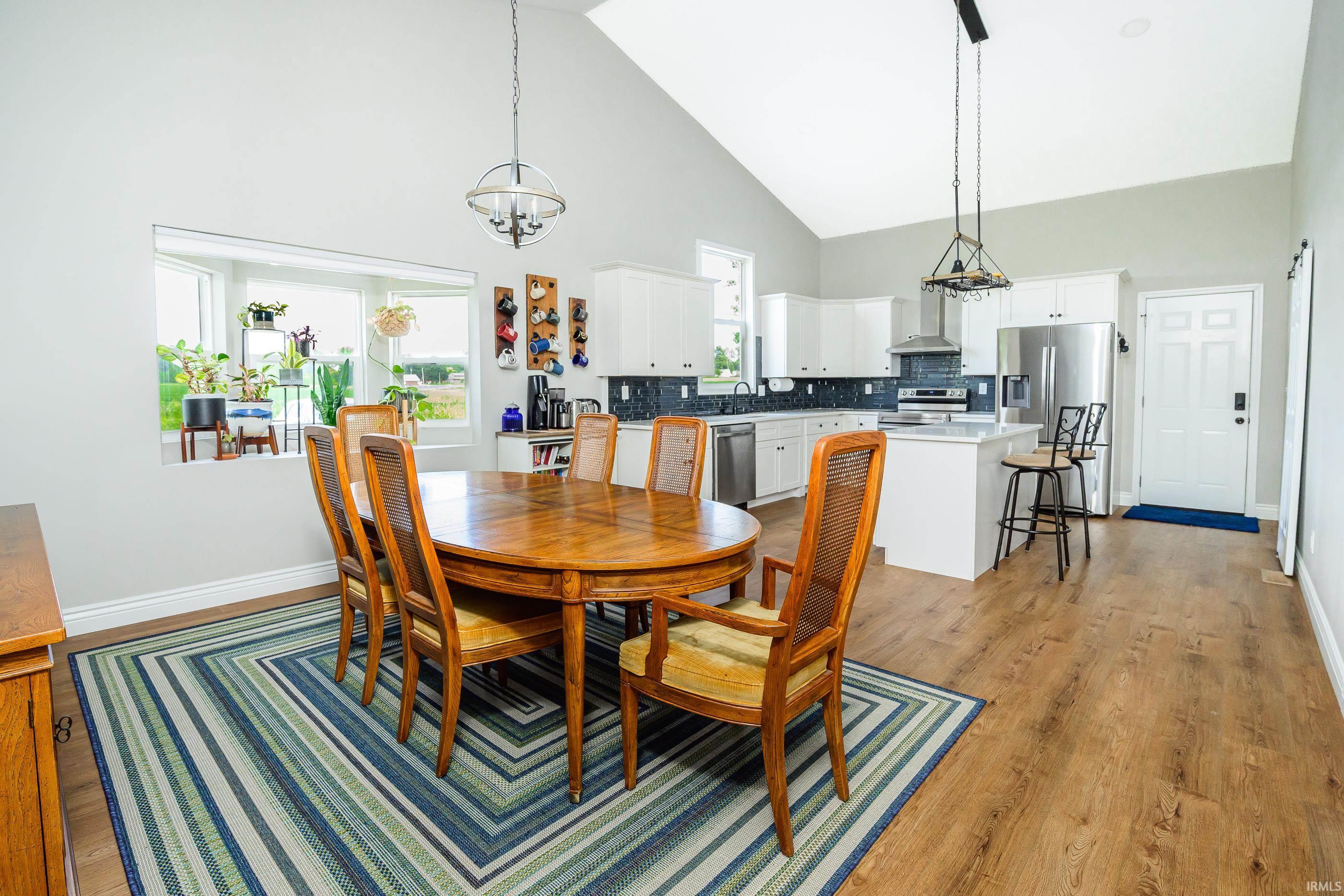 Dining area with a wood table and striped rug opens to a bright kitchen with white cabinets.