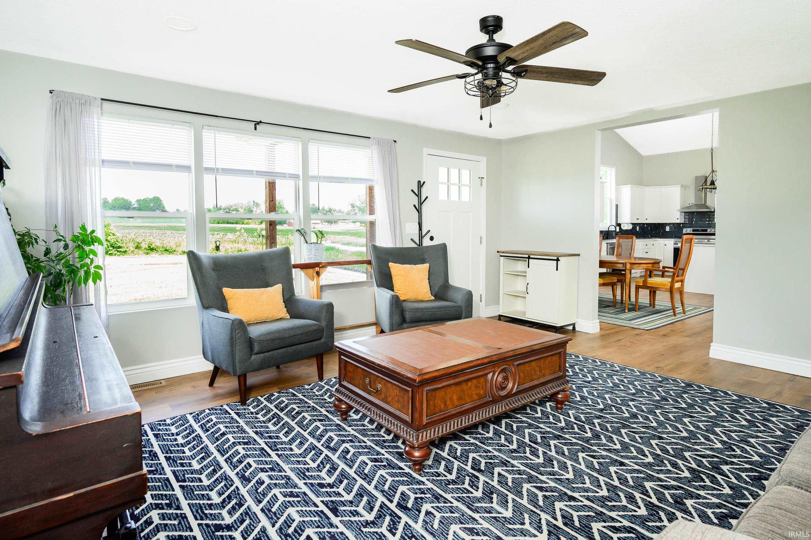 Furnished living room with gray armchairs, a carved coffee table, and windows overlooking open fields.