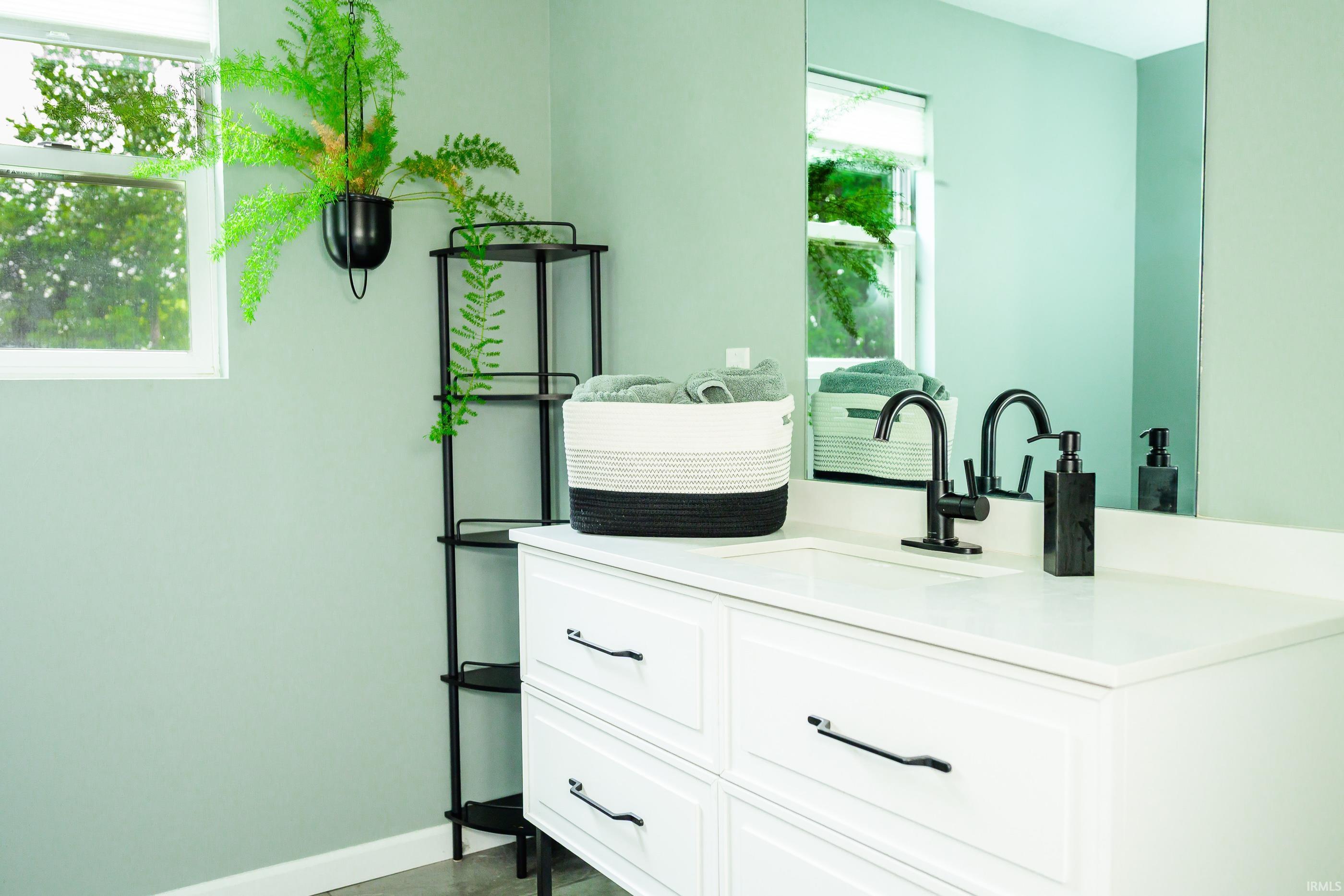 Bathroom vanity with black fixtures, a mirrored wall, folded towels, and a hanging plant.