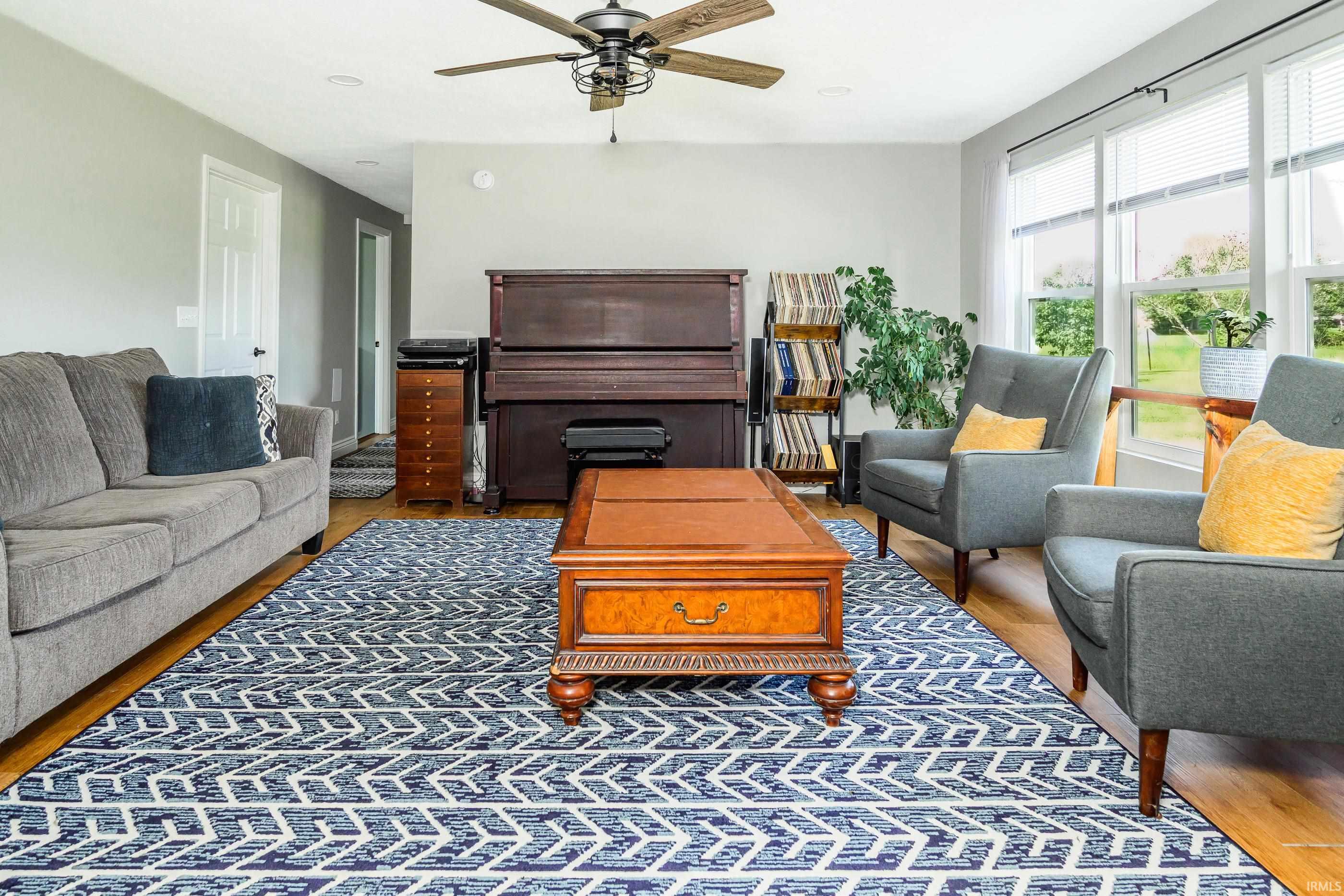 Furnished living room with an upright piano, tall windows, and a blue-and-white patterned rug.