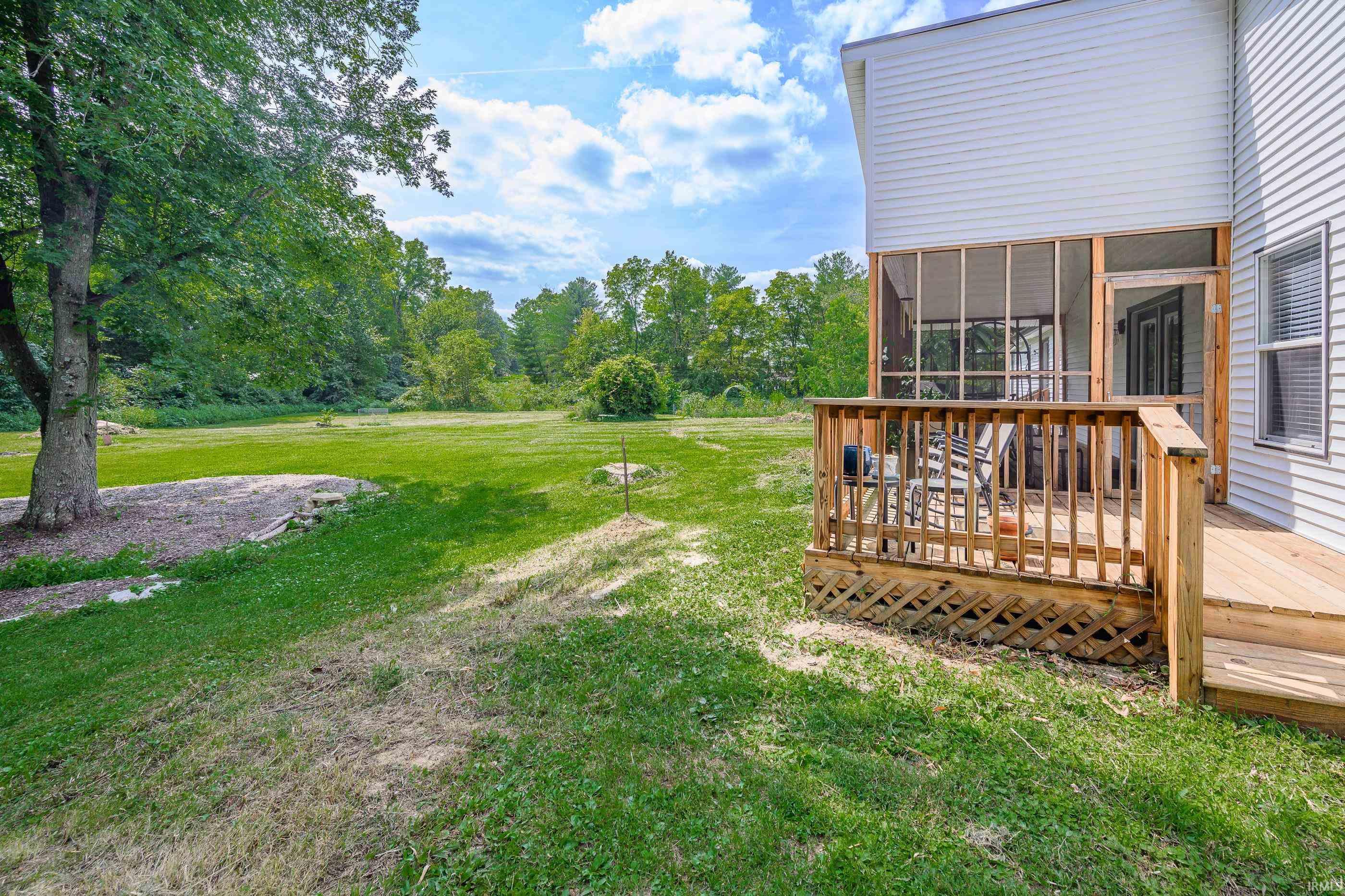Home’s screened porch and wooden deck overlook a broad lawn bordered by mature trees.
