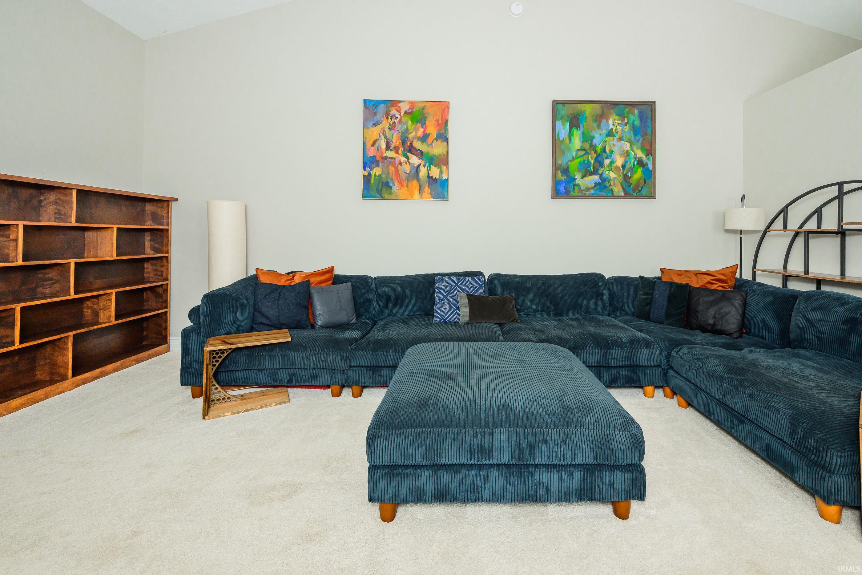Living room with a dark teal sectional sofa, matching ottoman, wooden shelving, and colorful wall art.