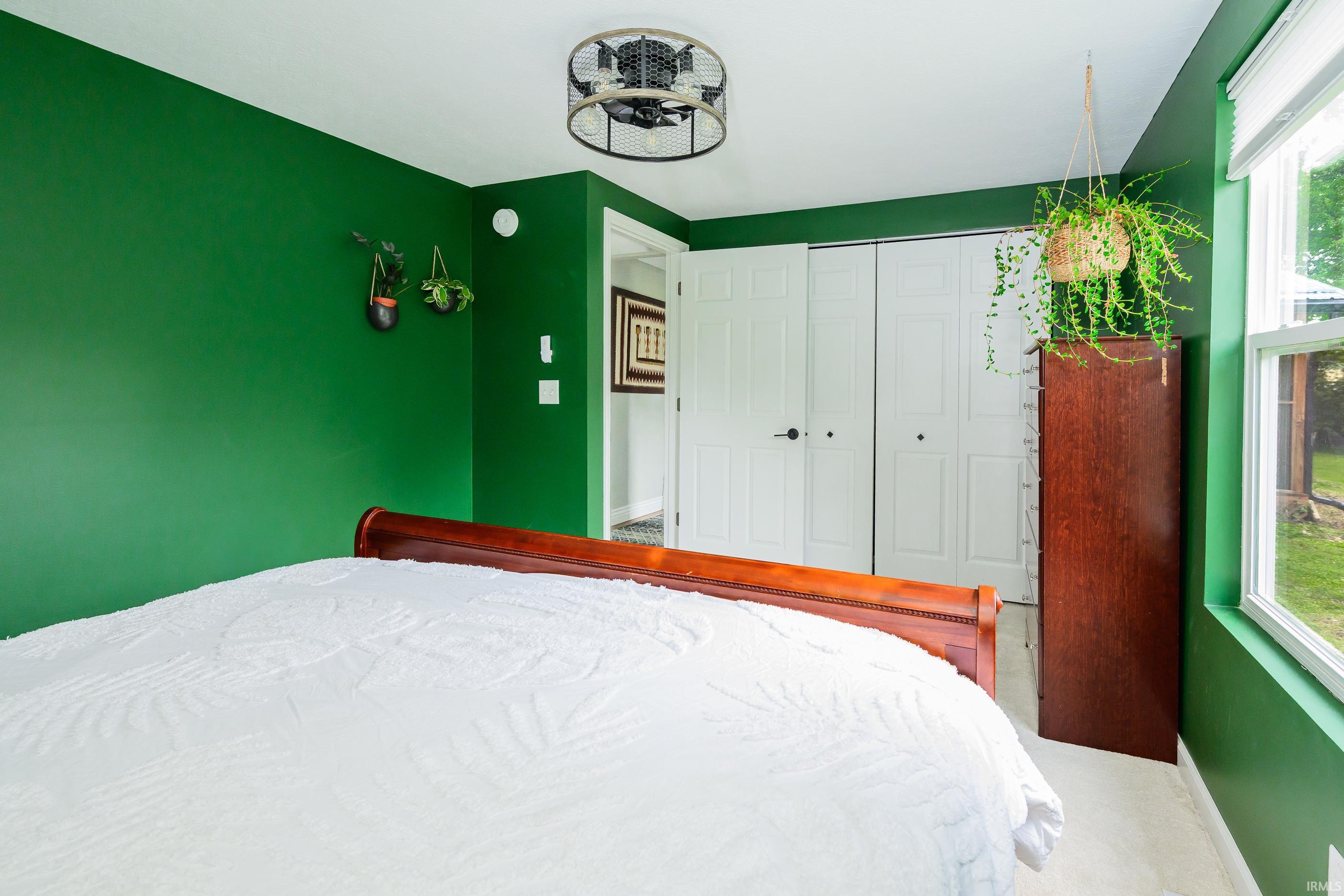 Bedroom with deep green walls, white bedding, wooden furniture, and a bright window.