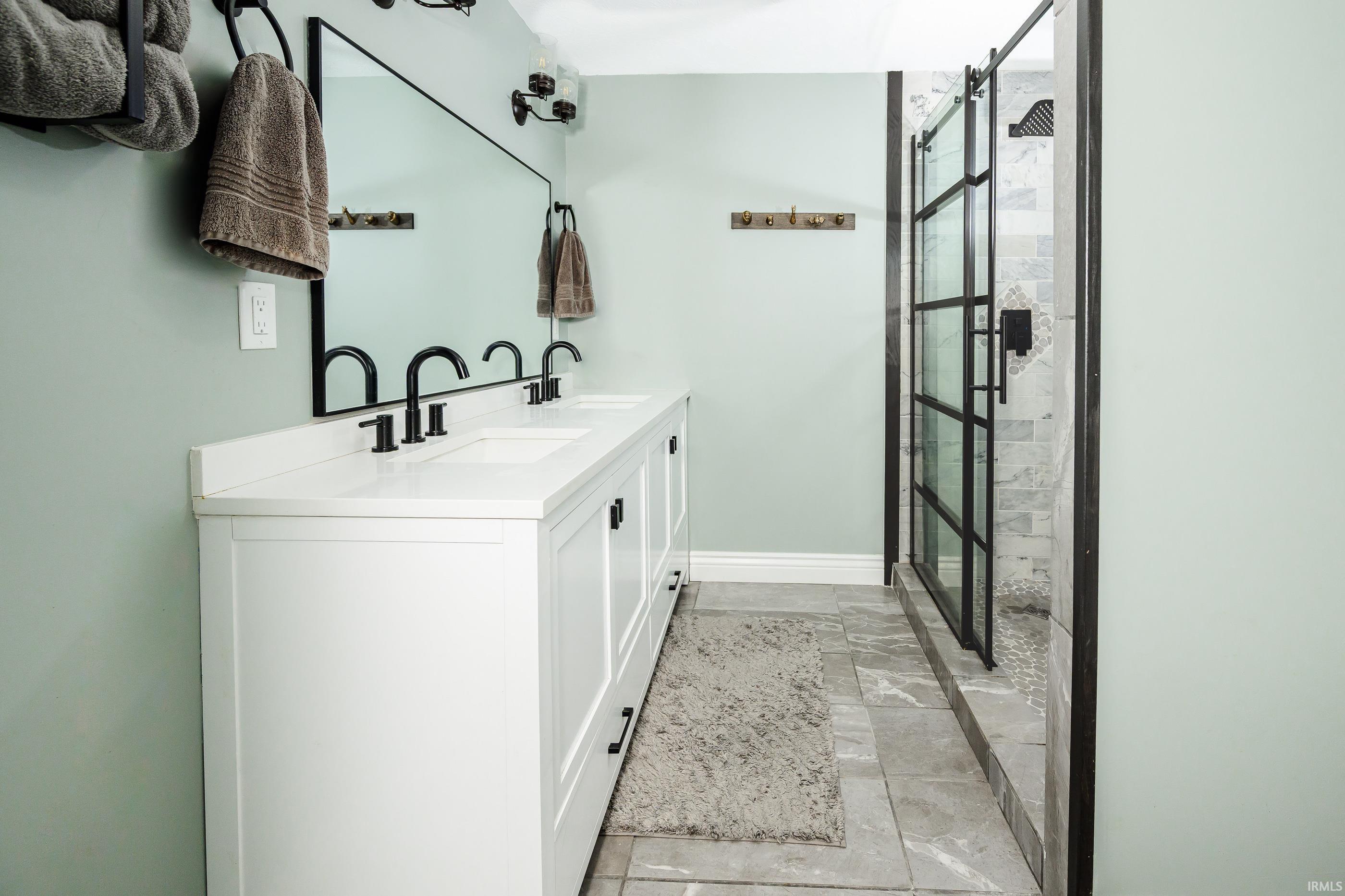 Bathroom with a white double vanity and black-framed glass shower with marble-look tile.