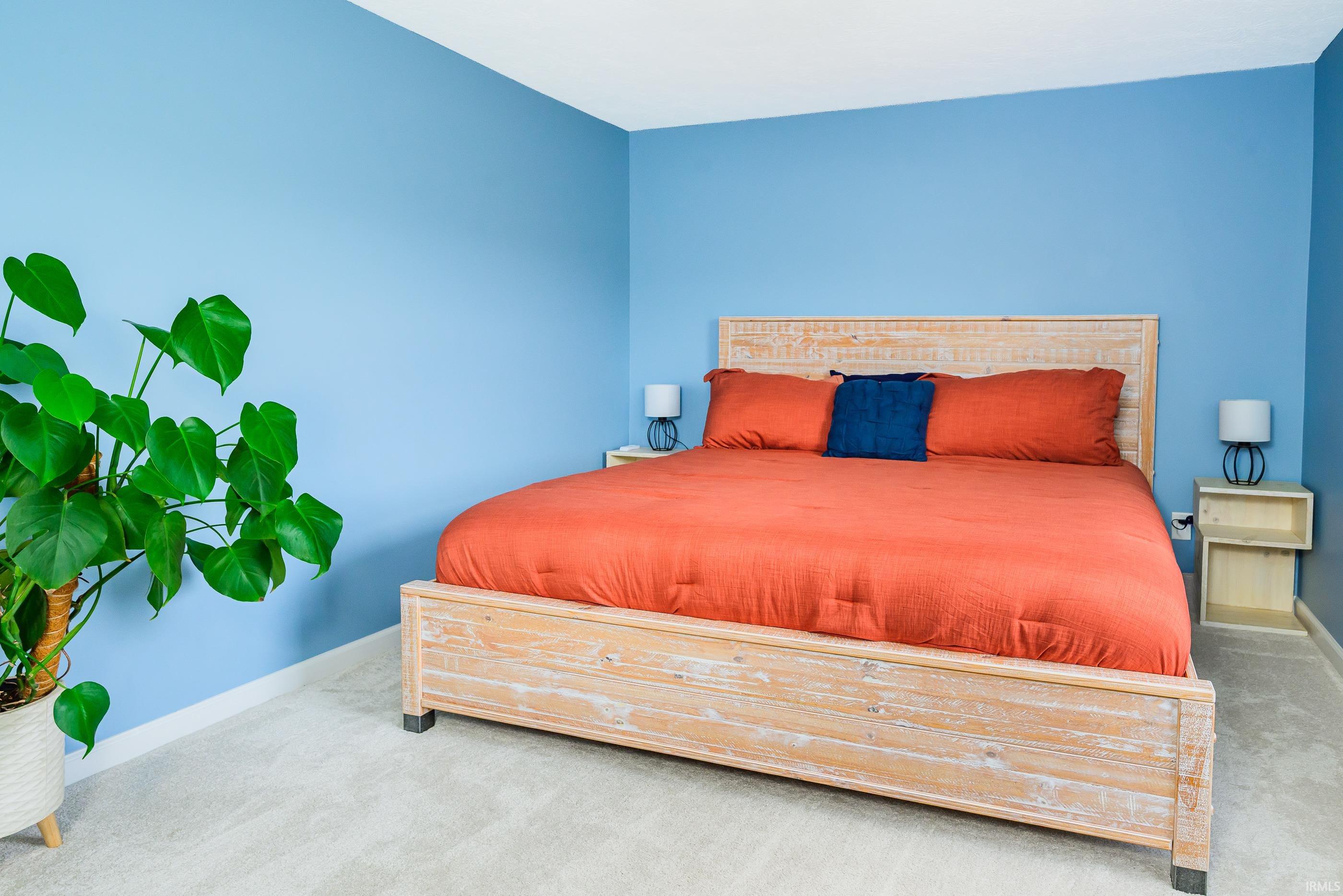 Blue bedroom with a distressed wood bed, coral bedding, navy pillow, and large potted plant.