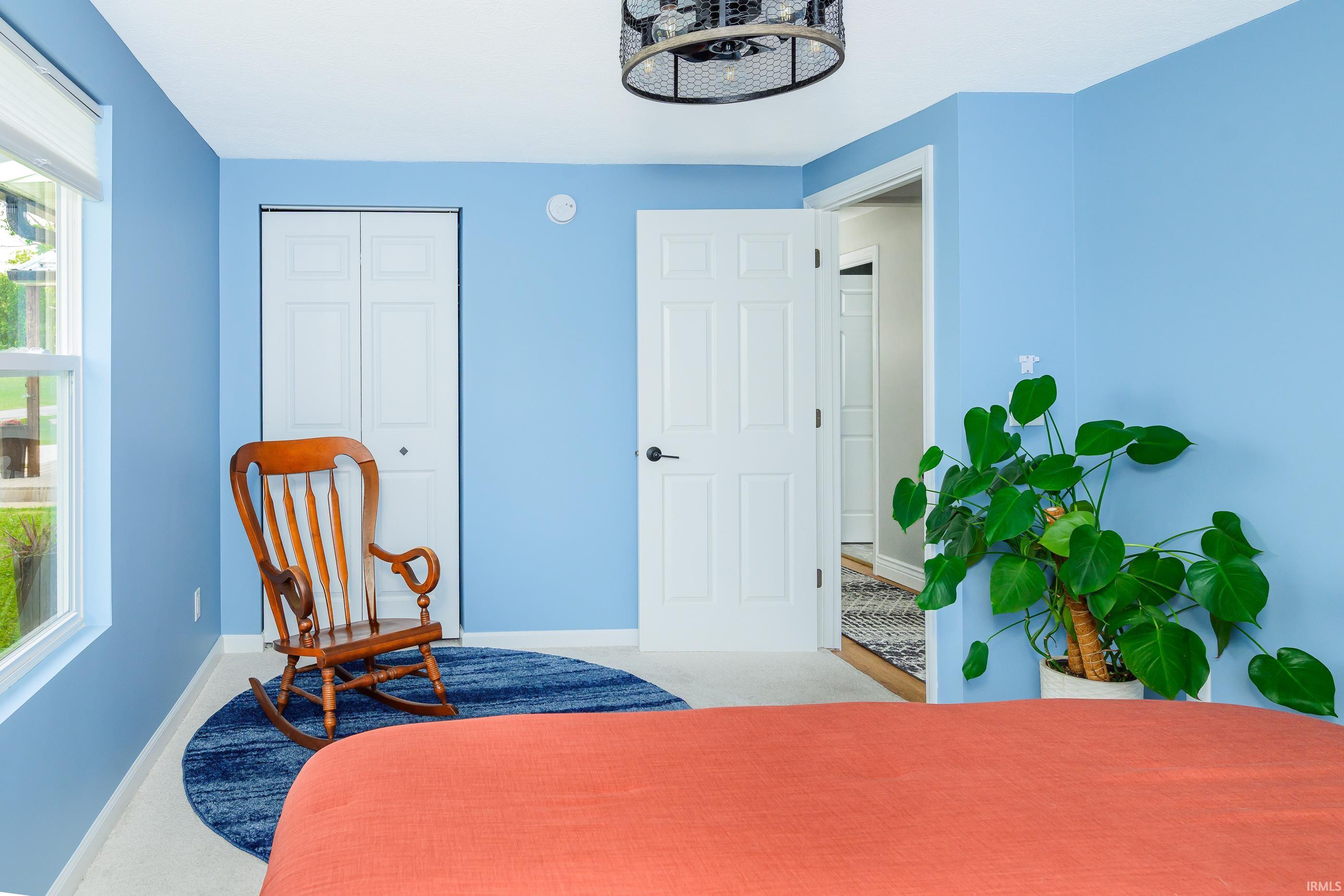 Blue bedroom with coral bedspread, wooden rocking chair, and leafy potted plant.