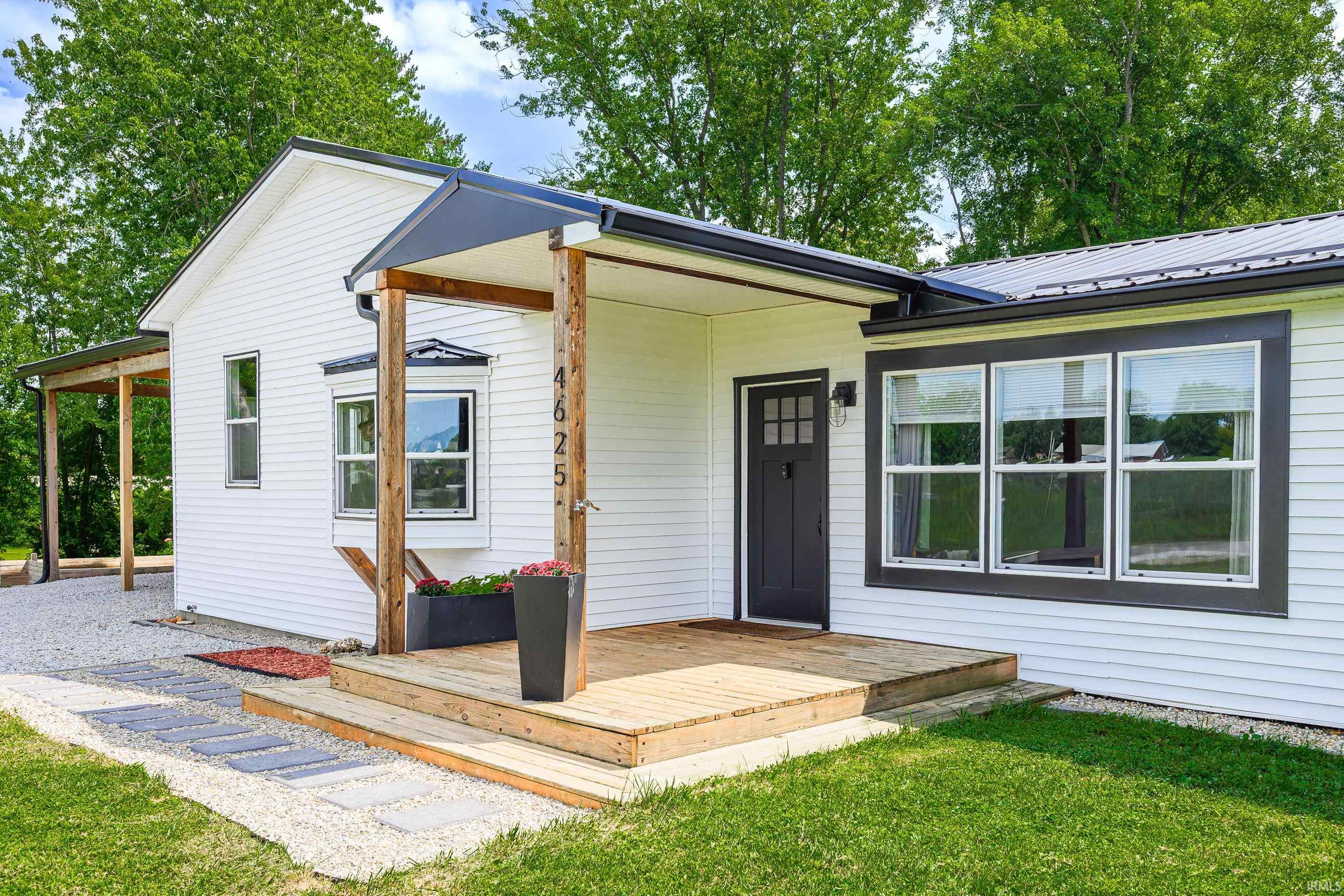 White-sided home with dark trim, a covered wooden porch, and flower planters.