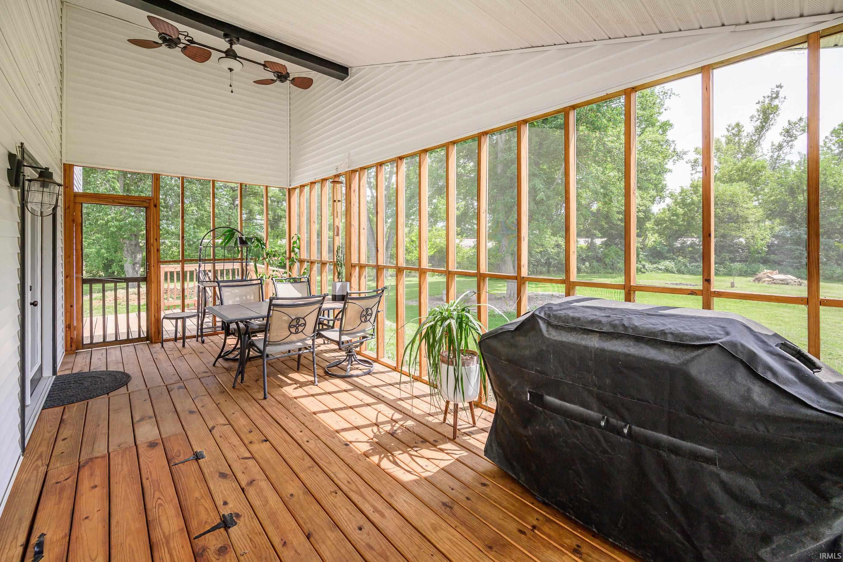 Enclosed sunroom with wood floors, tall screened windows, dining set, and covered grill.