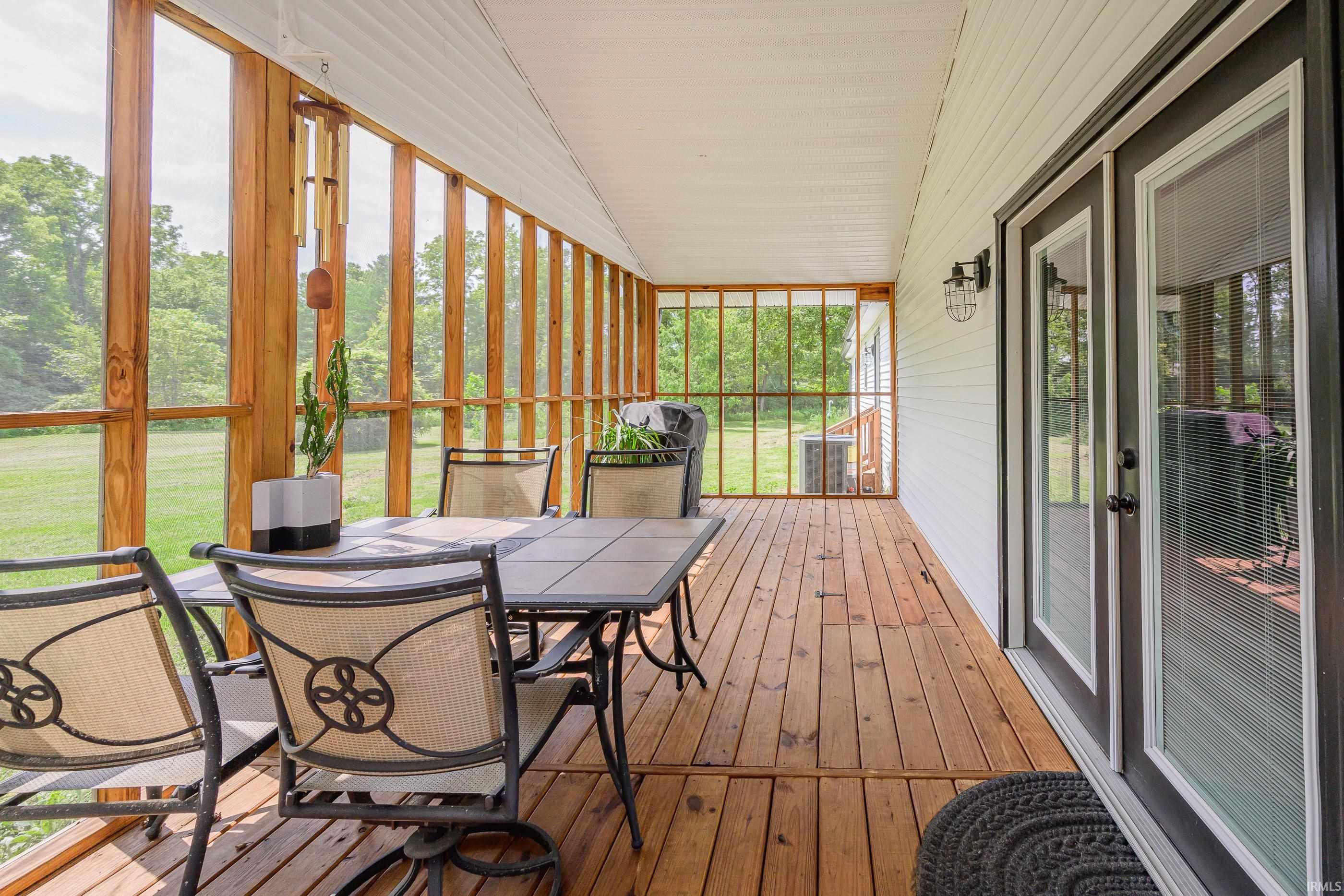 Screened porch with wood flooring, patio dining set, and views of a green lawn and trees.