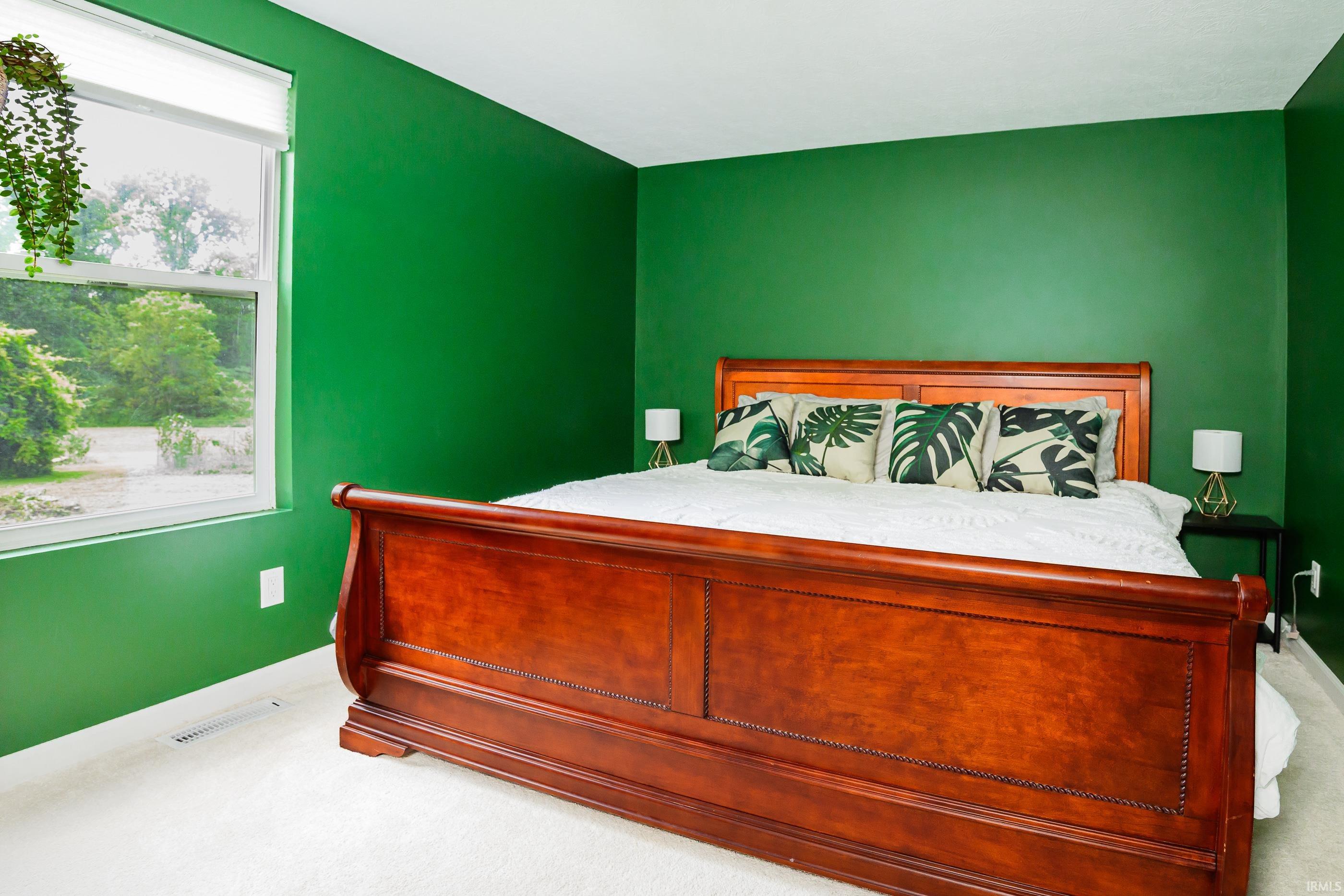 Bedroom with green walls, a large wooden bed, and leafy-patterned pillows beside a window.