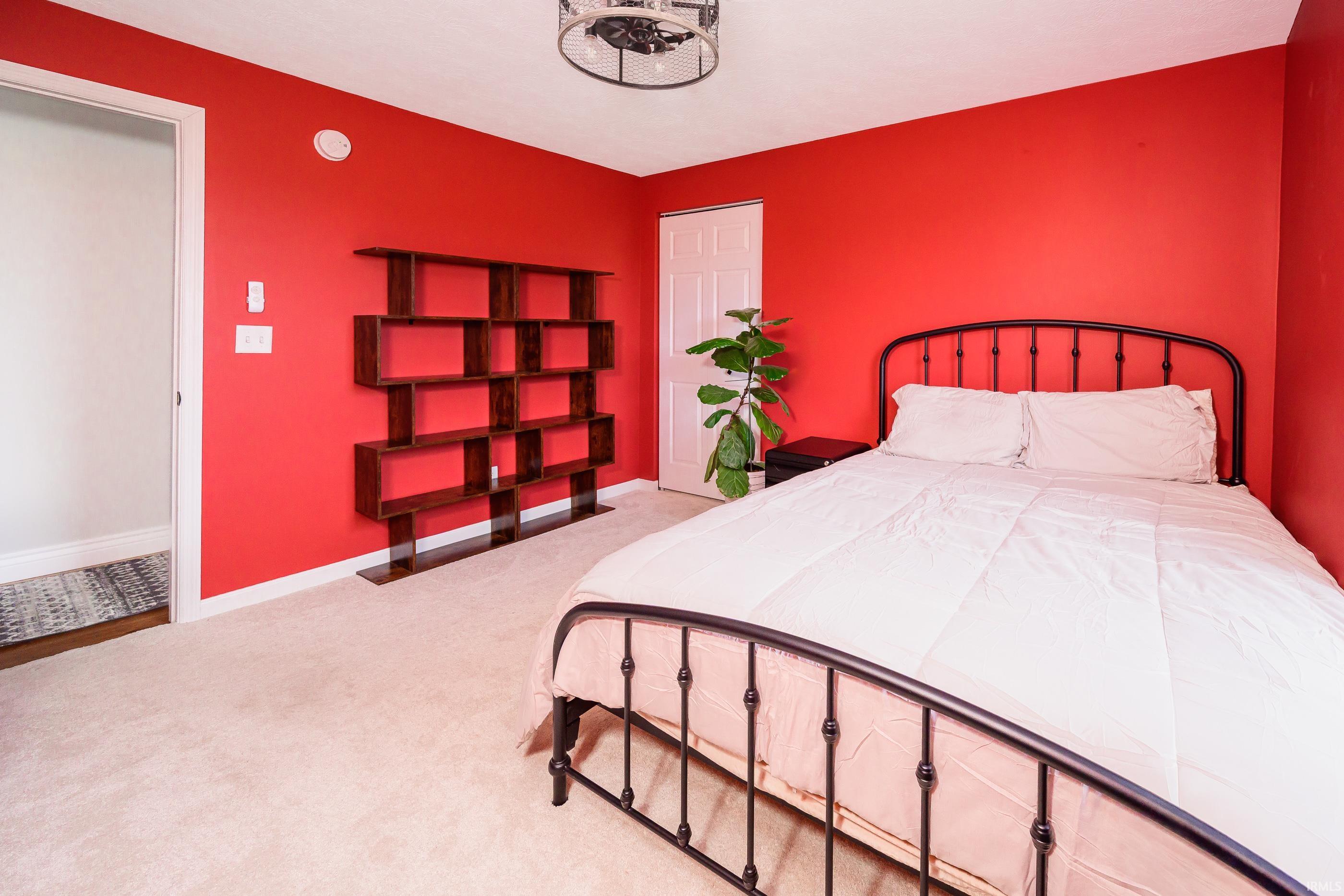 Bedroom with vivid red walls, a black metal bed, geometric shelving, and a potted plant.