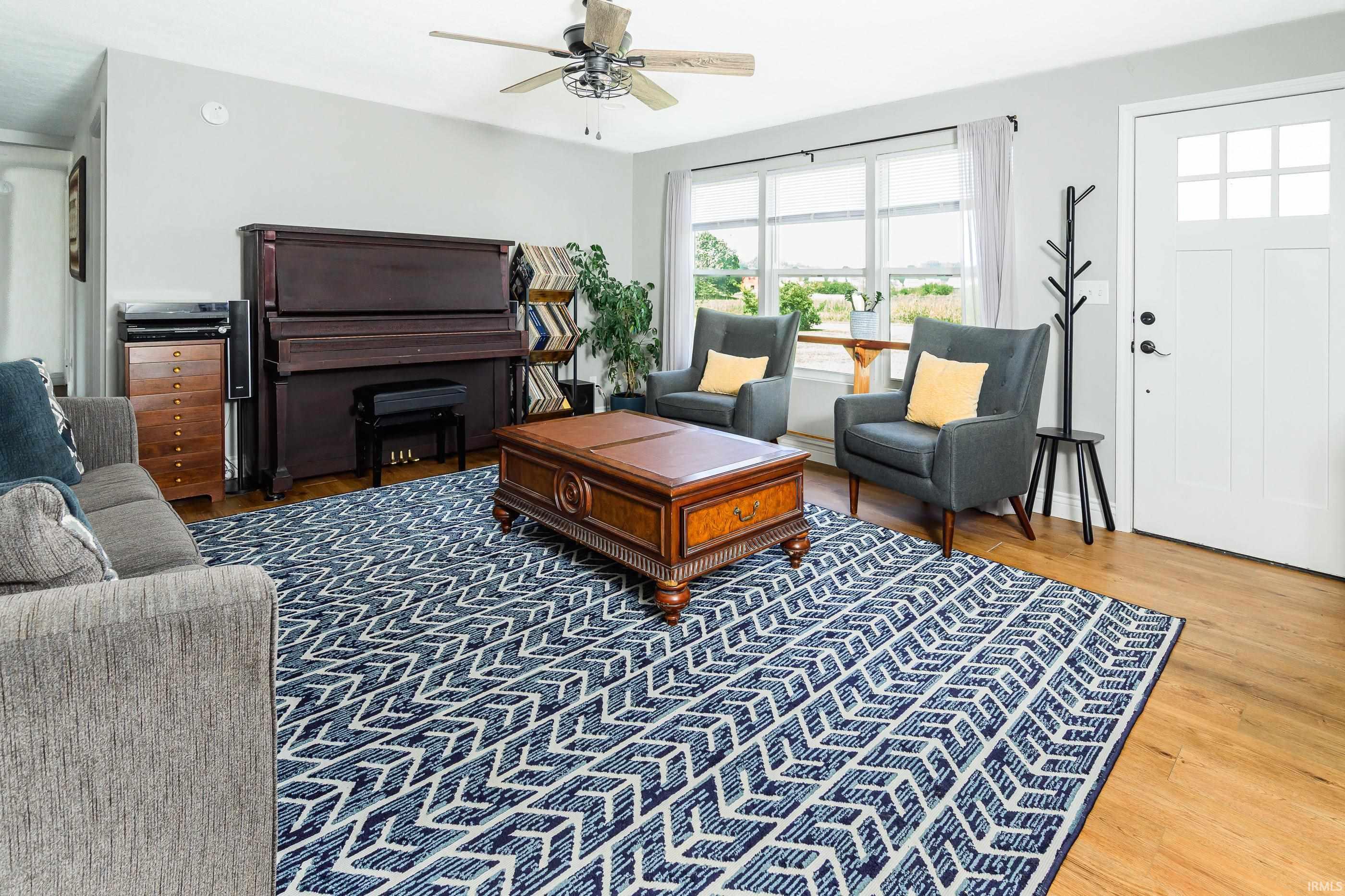 Living room with an upright piano, gray armchairs, and a large blue-and-white patterned rug.