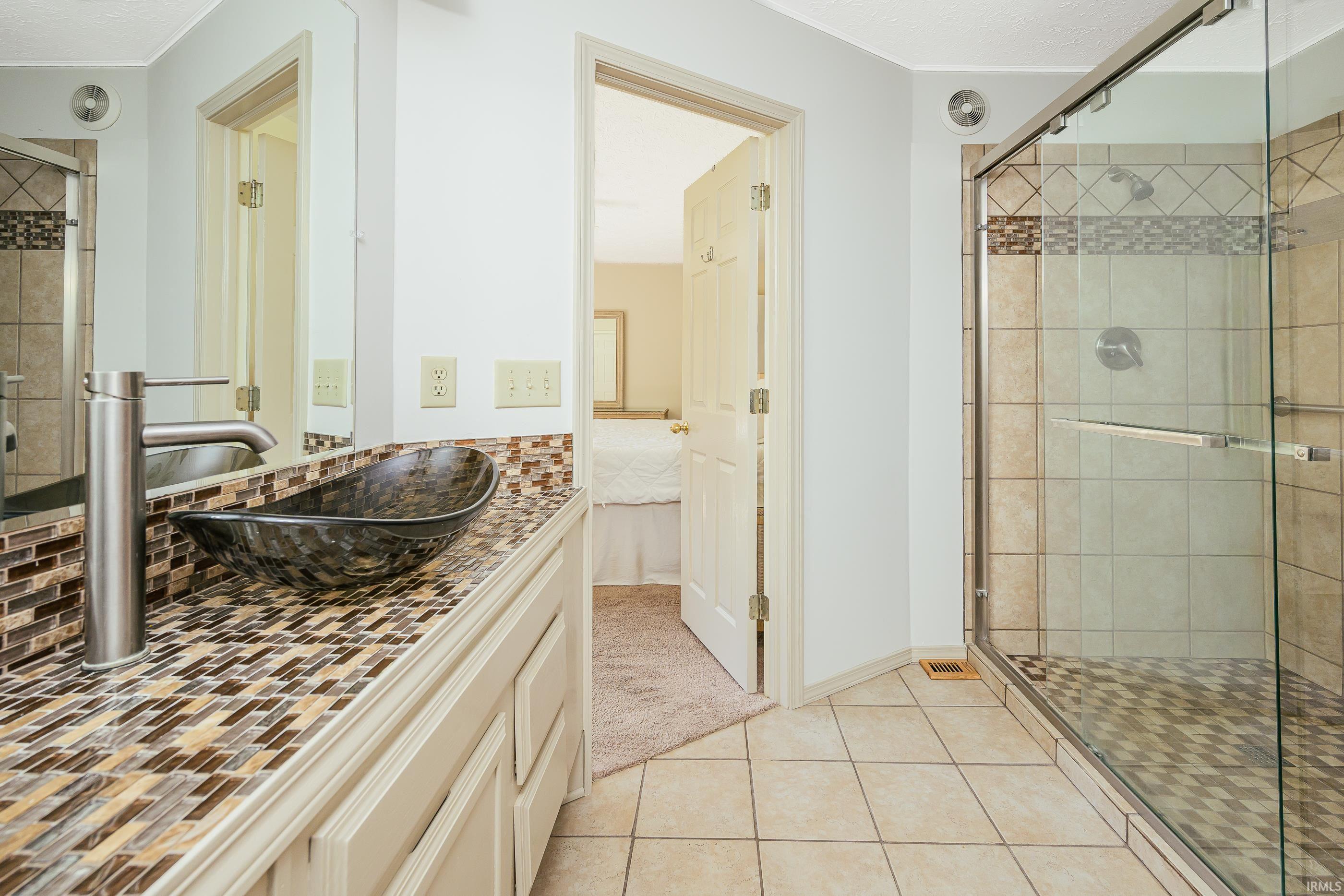 Bathroom with a glass-enclosed tiled shower and a dark vessel sink on a mosaic-tile vanity.