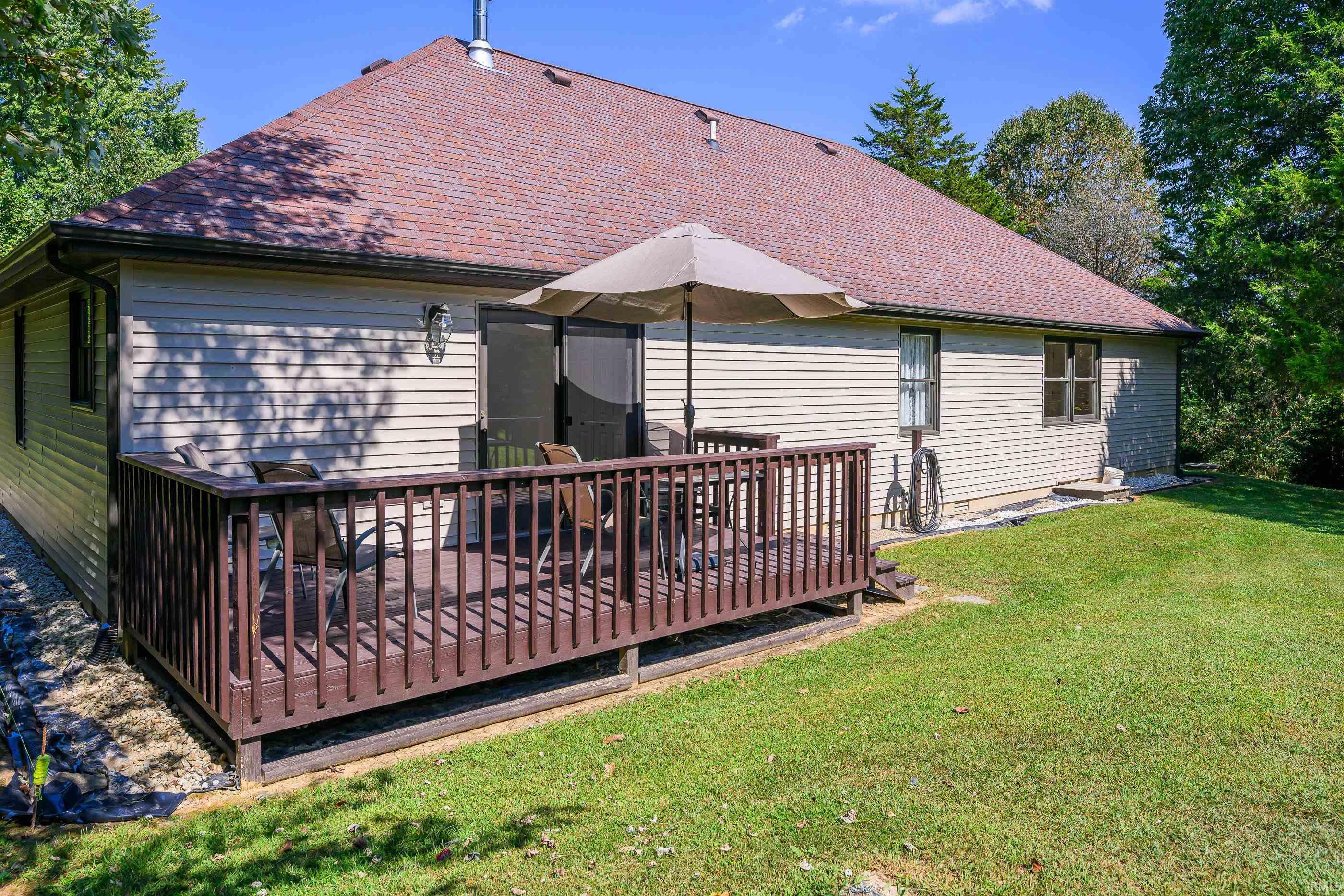 Home’s rear exterior with a raised wooden deck, patio chairs, and umbrella beside a green lawn.