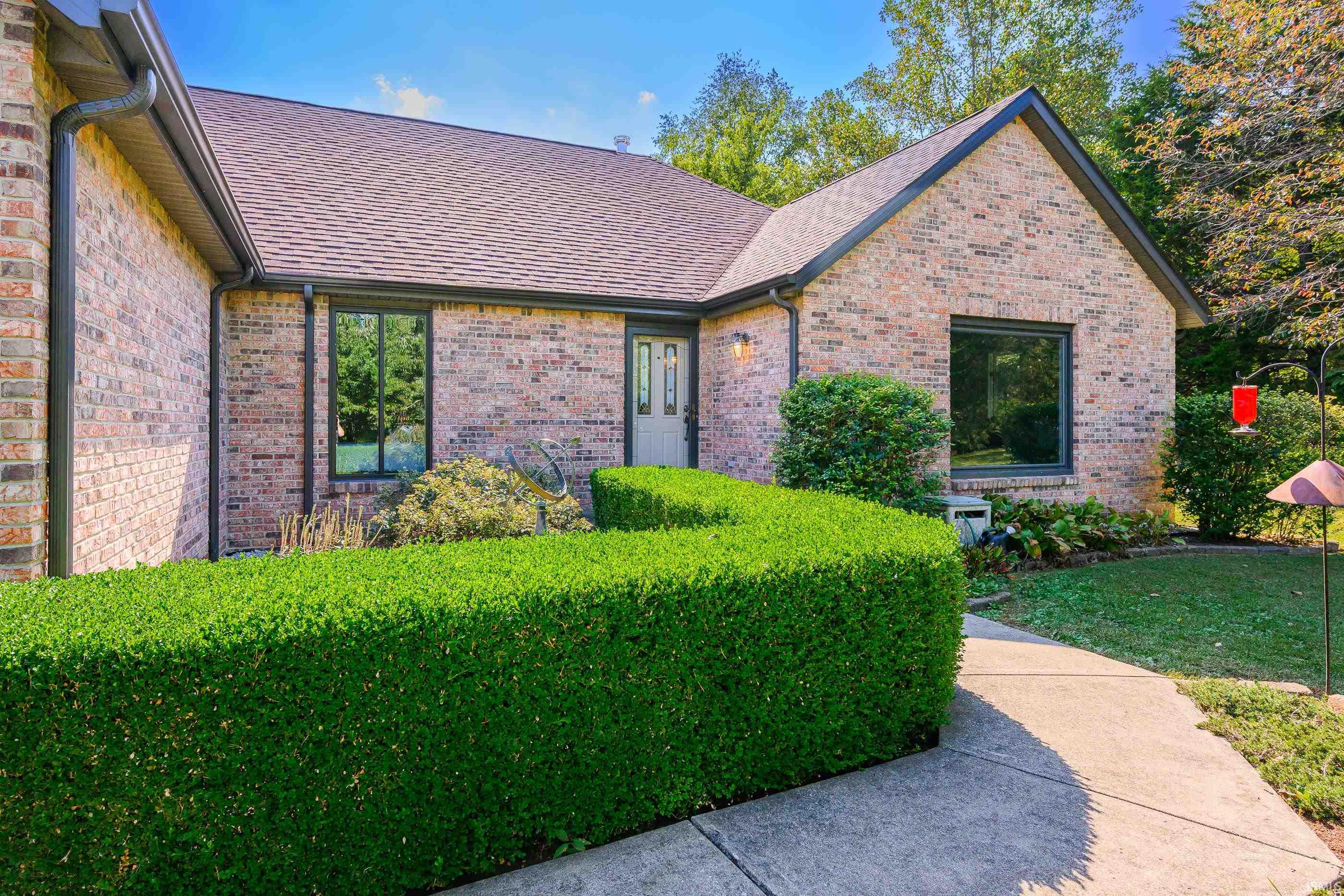Brick house with a gabled roof, trimmed hedges, and a curved concrete walkway to the entrance.
