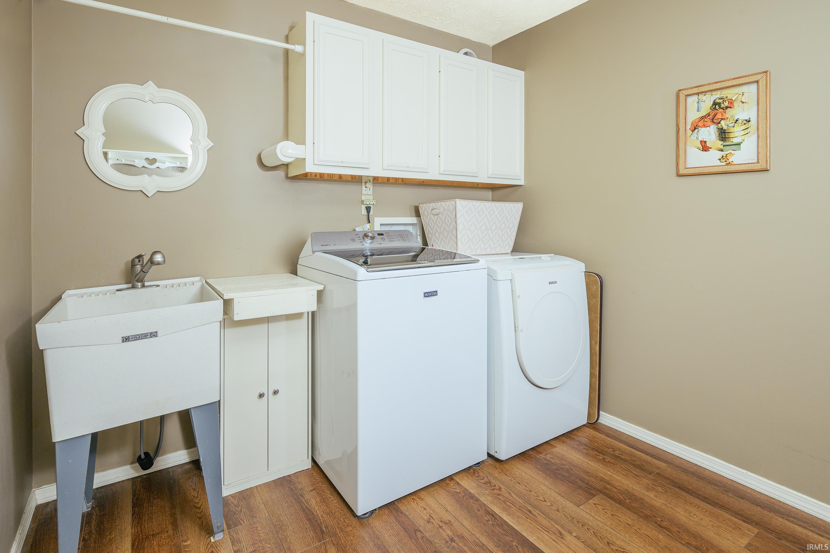 Laundry room with a utility sink, washer, dryer, and white wall cabinets.