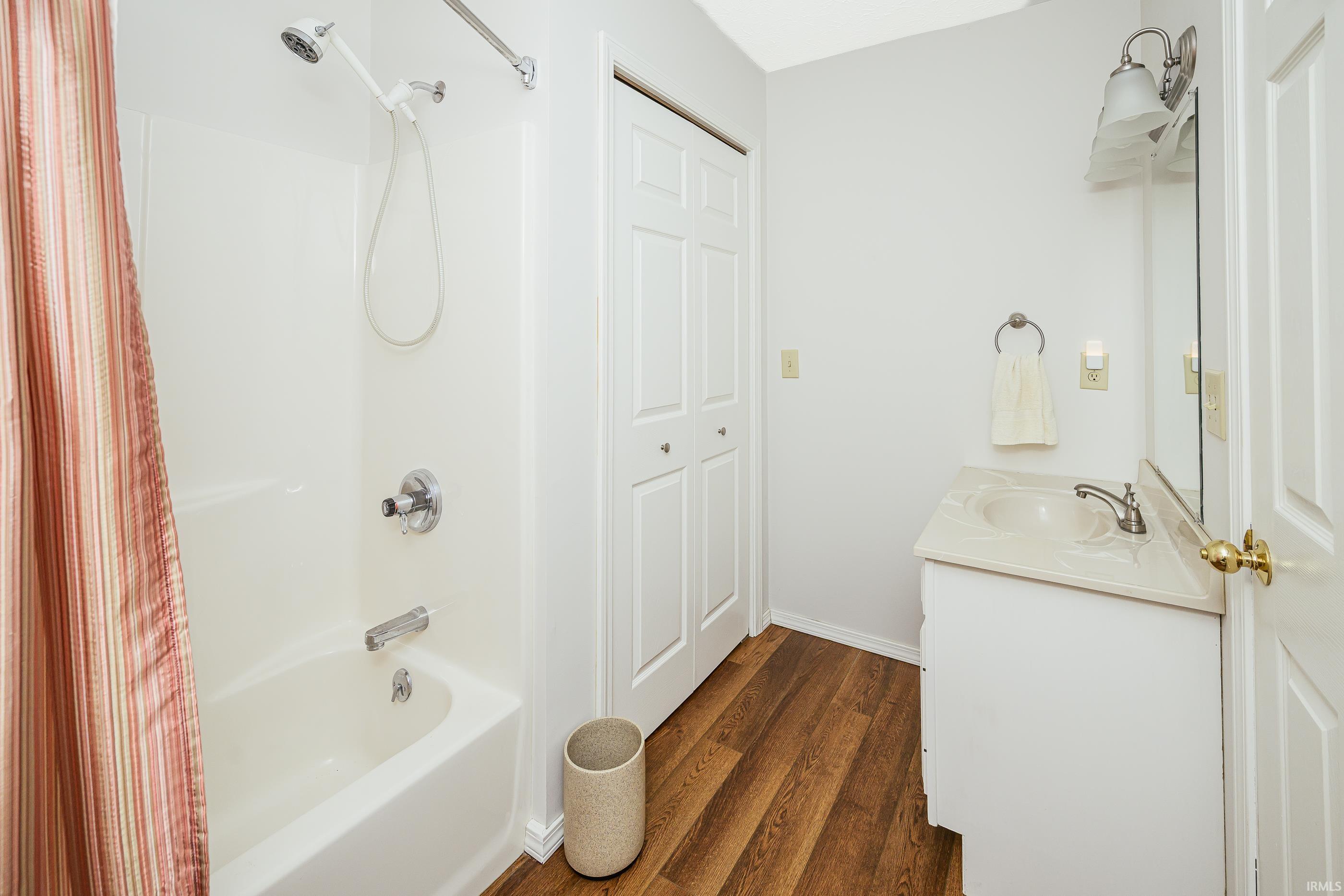 Bathroom with a striped shower curtain, white tub and vanity, and dark wood-look flooring.