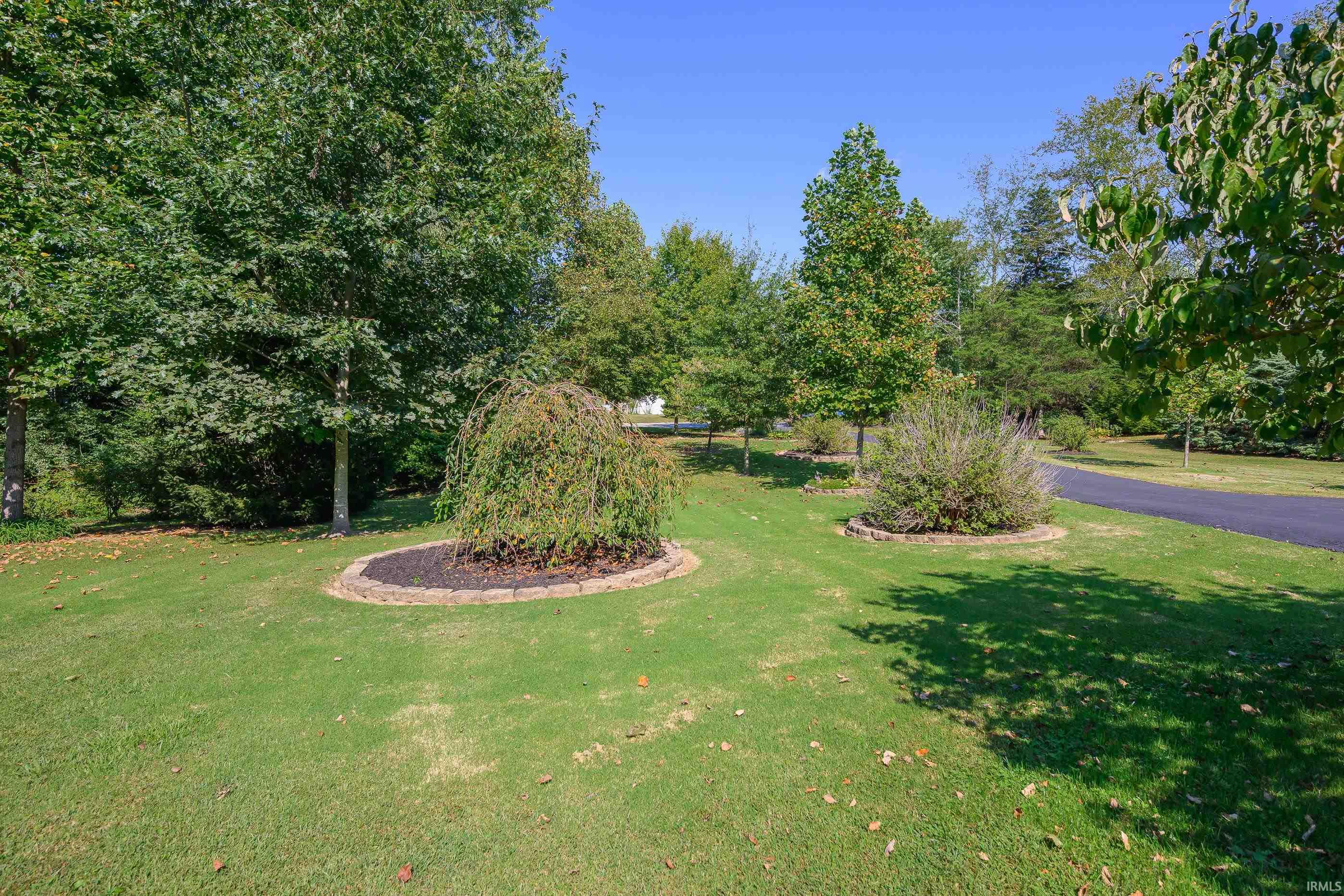 Landscaped lawn with mature trees, stone-edged planting beds, and a curved driveway.