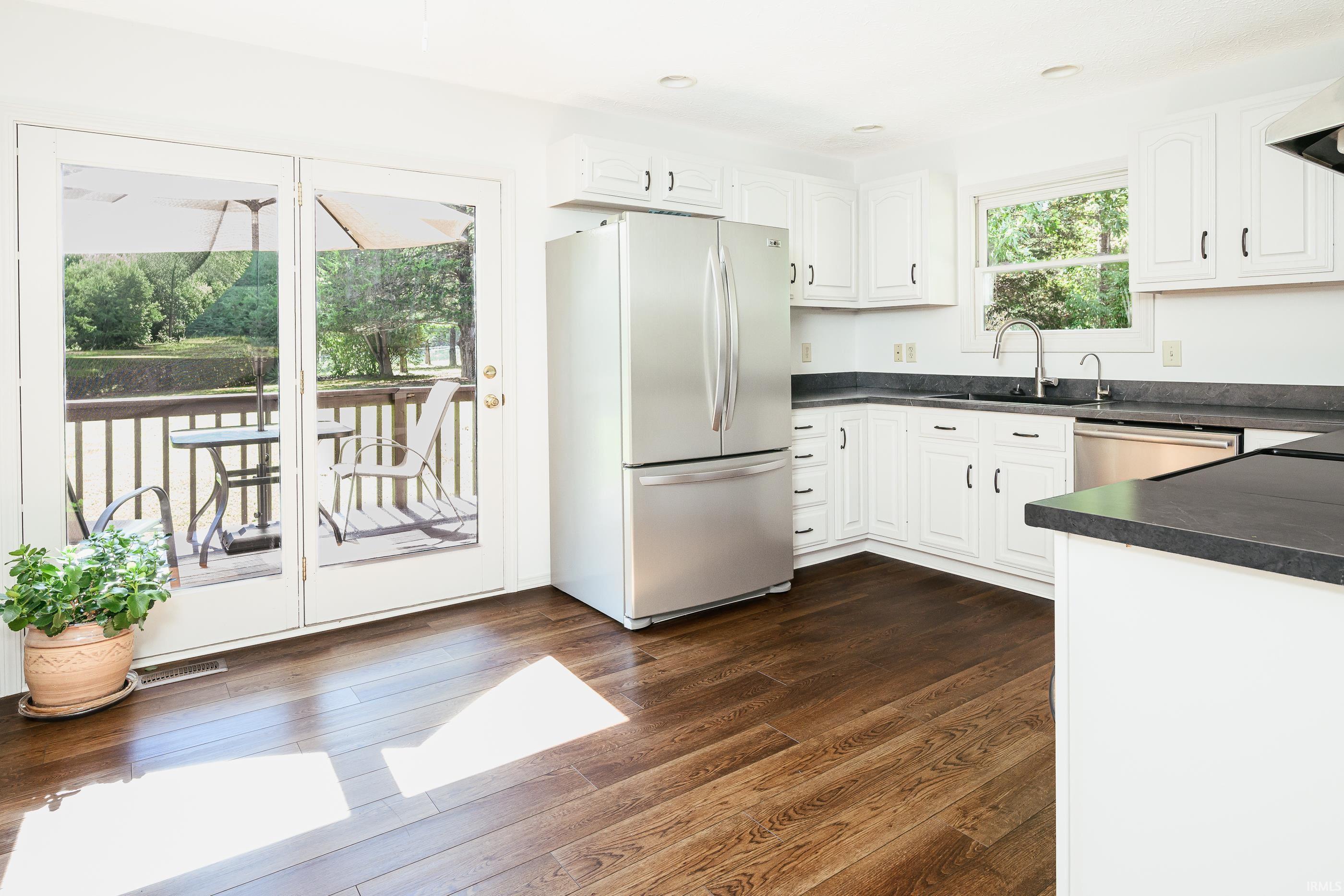 Bright white kitchen with stainless-steel appliances, dark wood floors, and French doors opening to a deck.