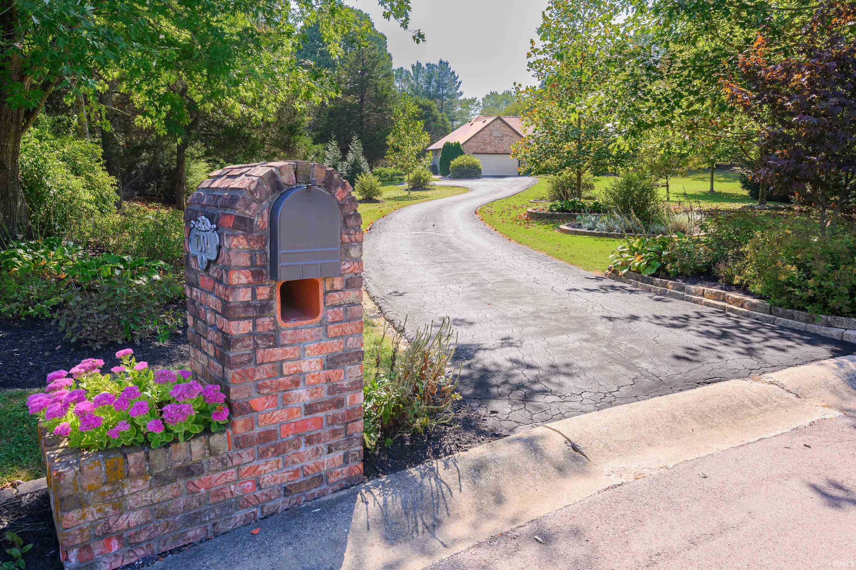 Brick mailbox marked 7004 beside a curved driveway leading to a tree-shaded home.