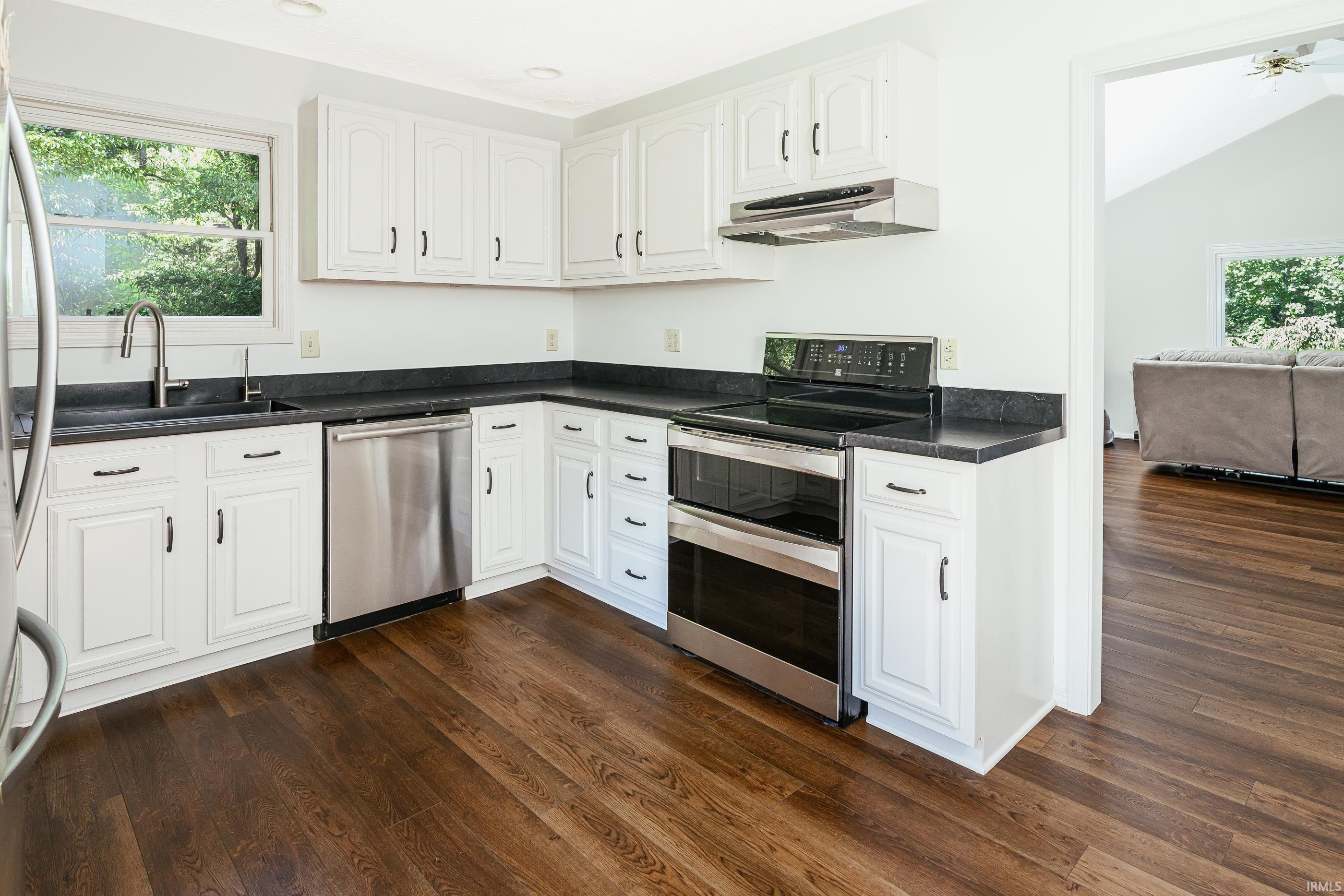 Kitchen with white cabinets, dark countertops, stainless-steel appliances, and dark wood floors.