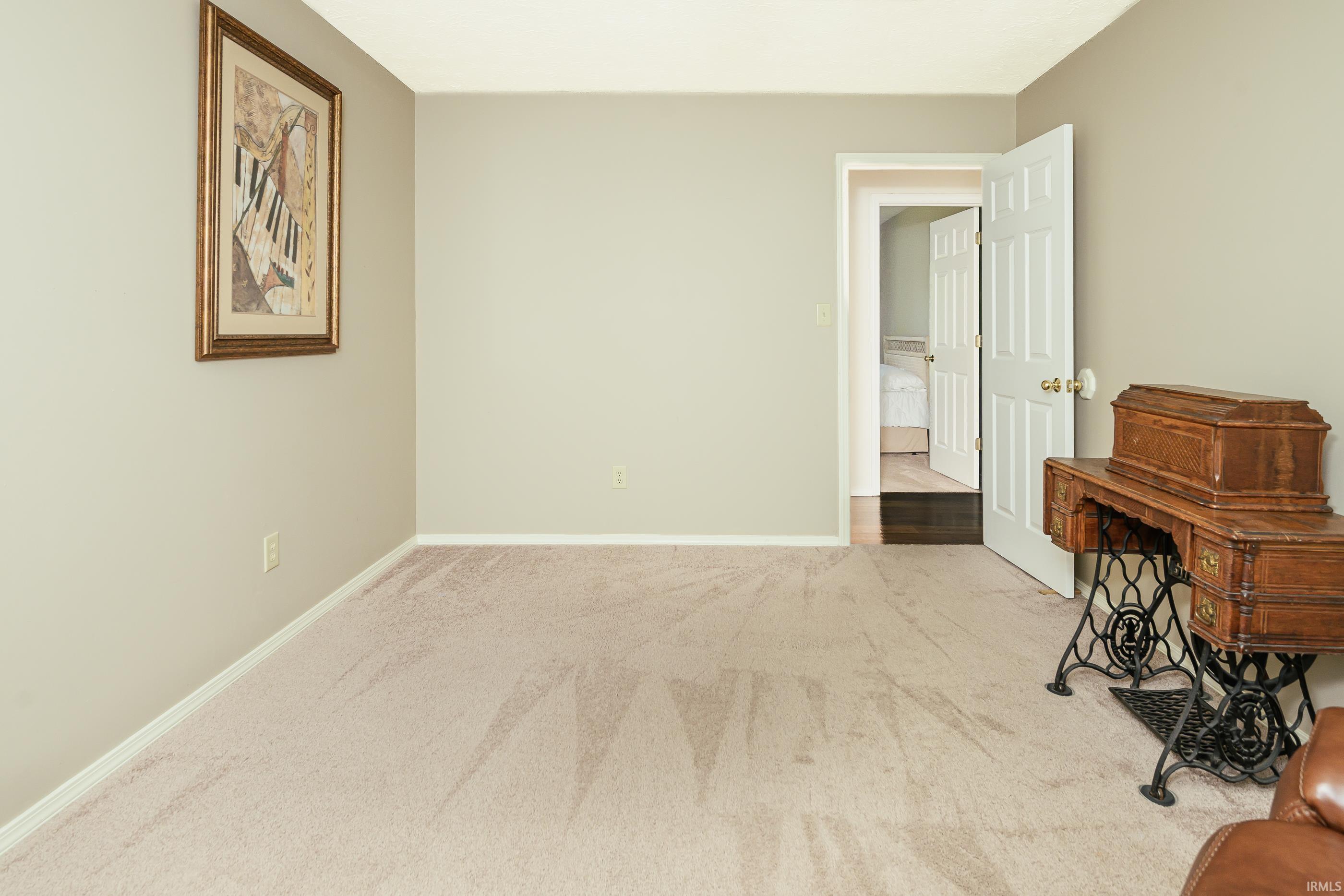 Carpeted room with framed artwork, an antique sewing machine cabinet, and an open bedroom doorway.