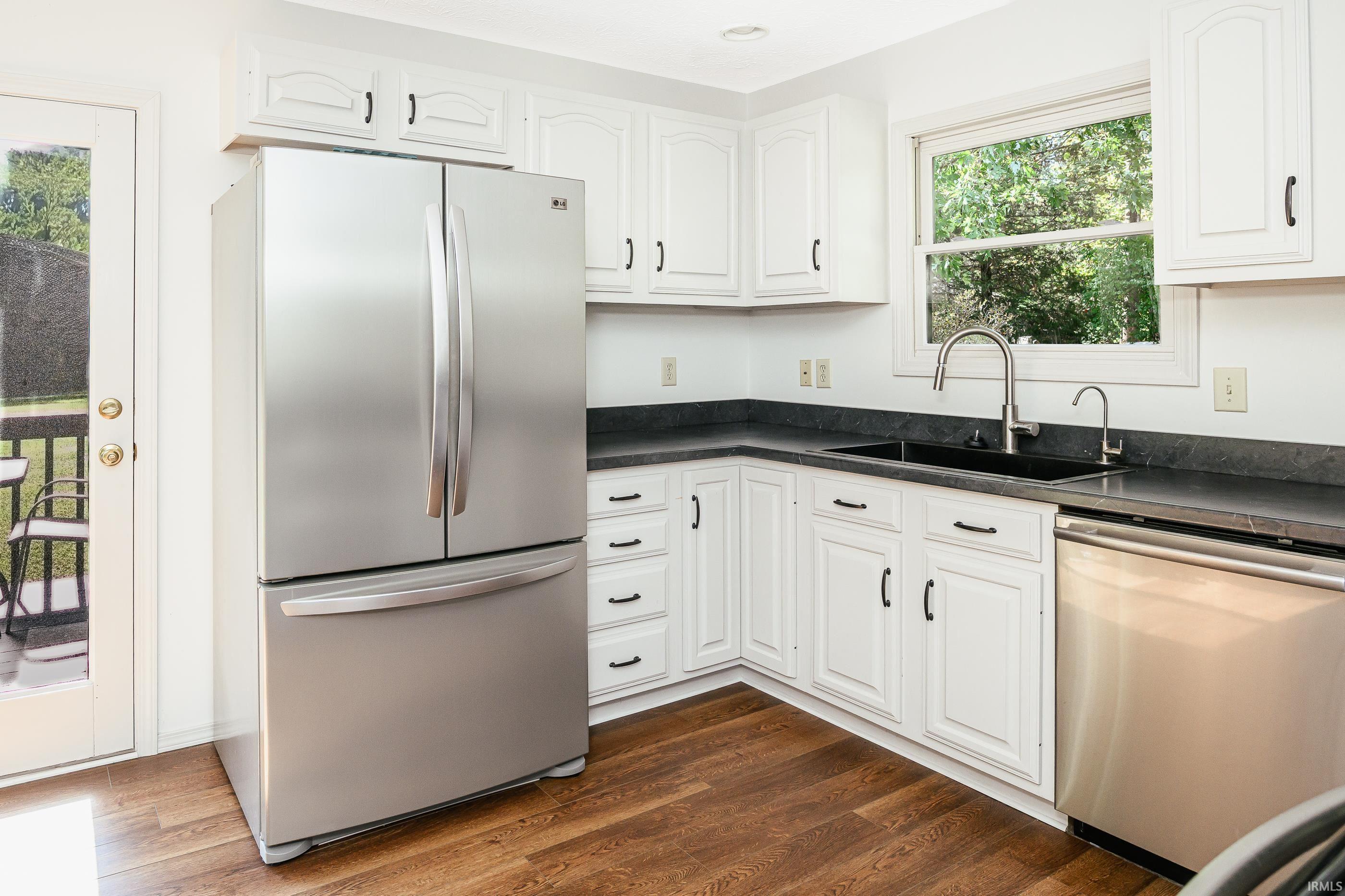 Kitchen with white cabinets, dark countertops, stainless steel appliances, and a window above the sink.