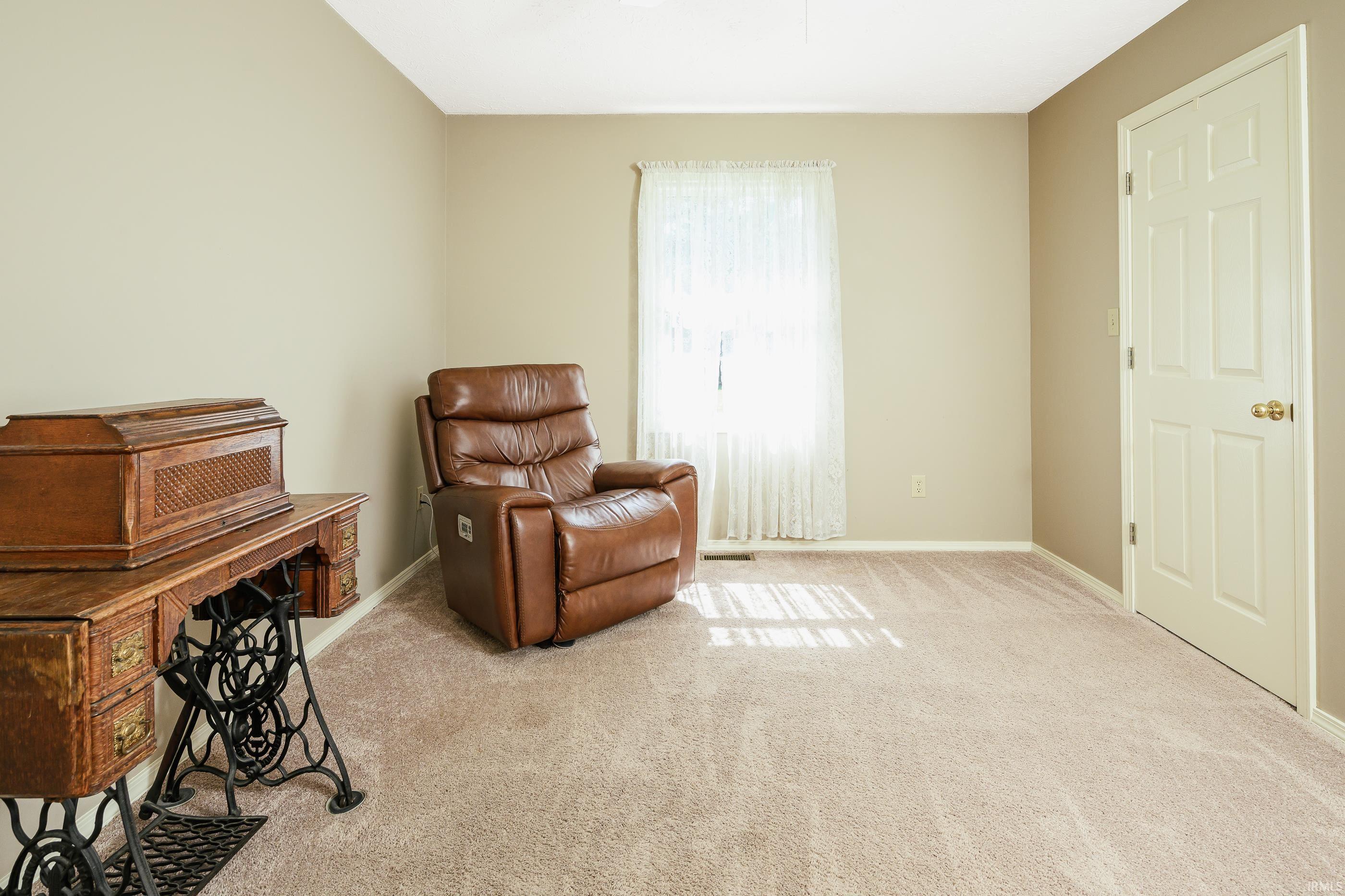 Carpeted room with a brown leather recliner, antique sewing machine cabinet, and lace-curtained window.