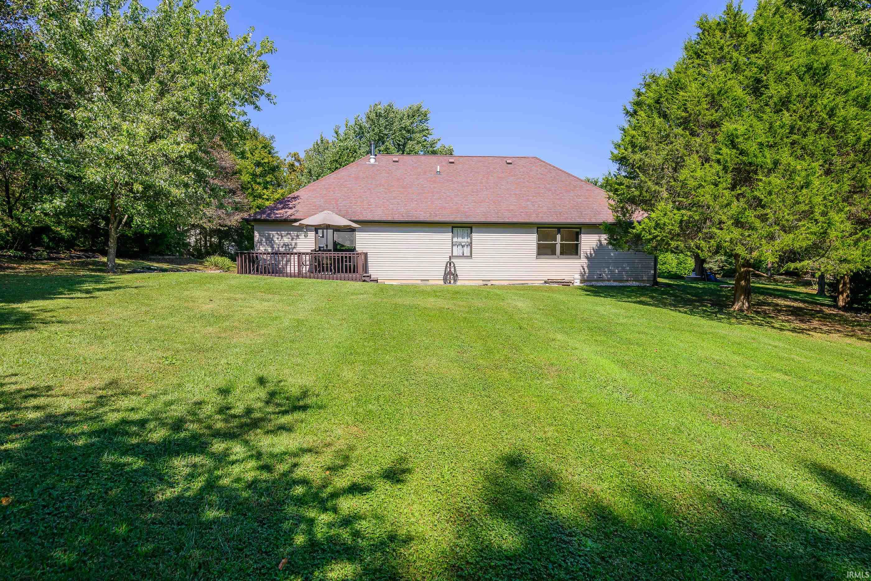 Rear of a single-story home across a broad lawn, with a raised deck and mature trees.