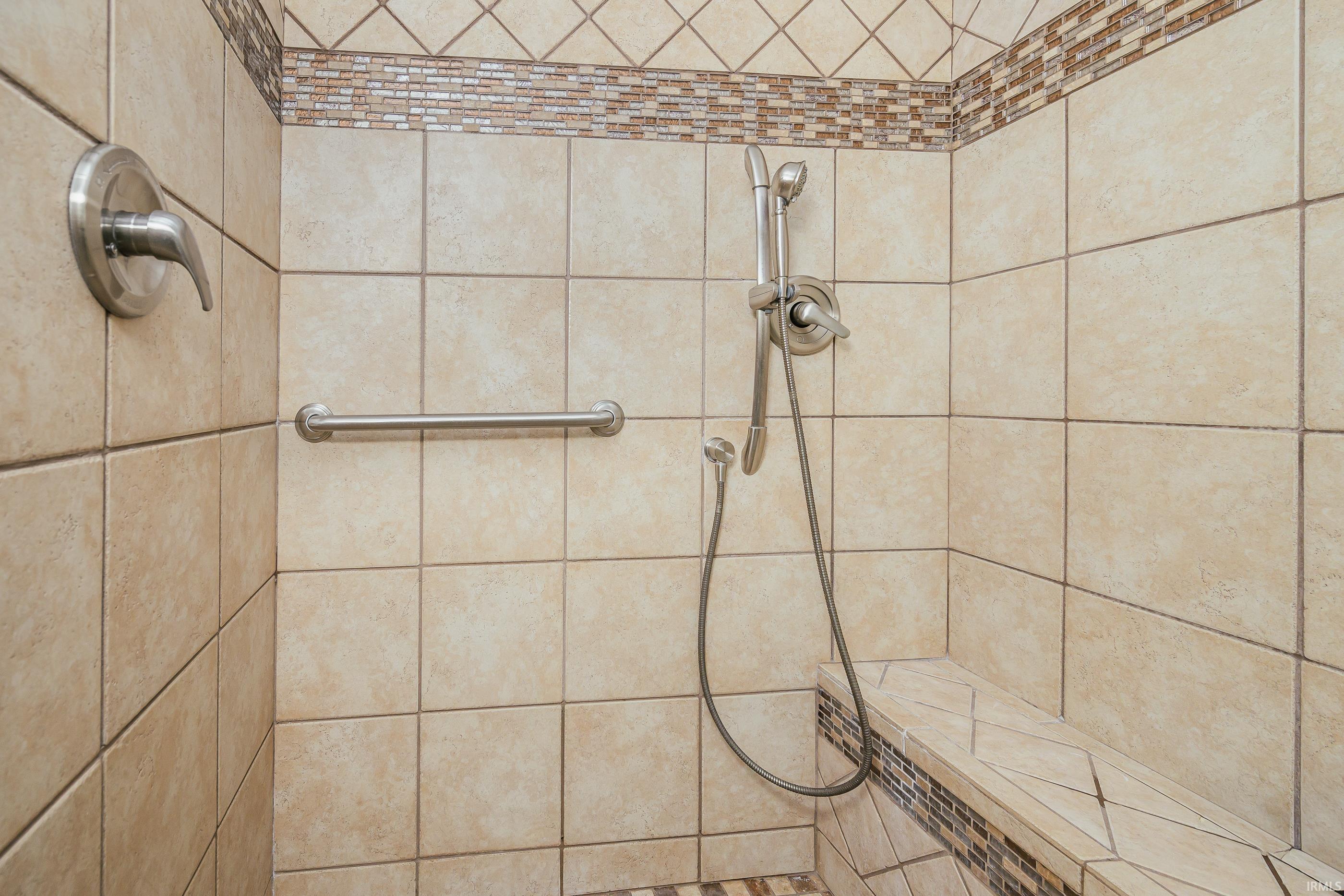 Tiled walk-in shower with a handheld showerhead, grab bar, and built-in bench.