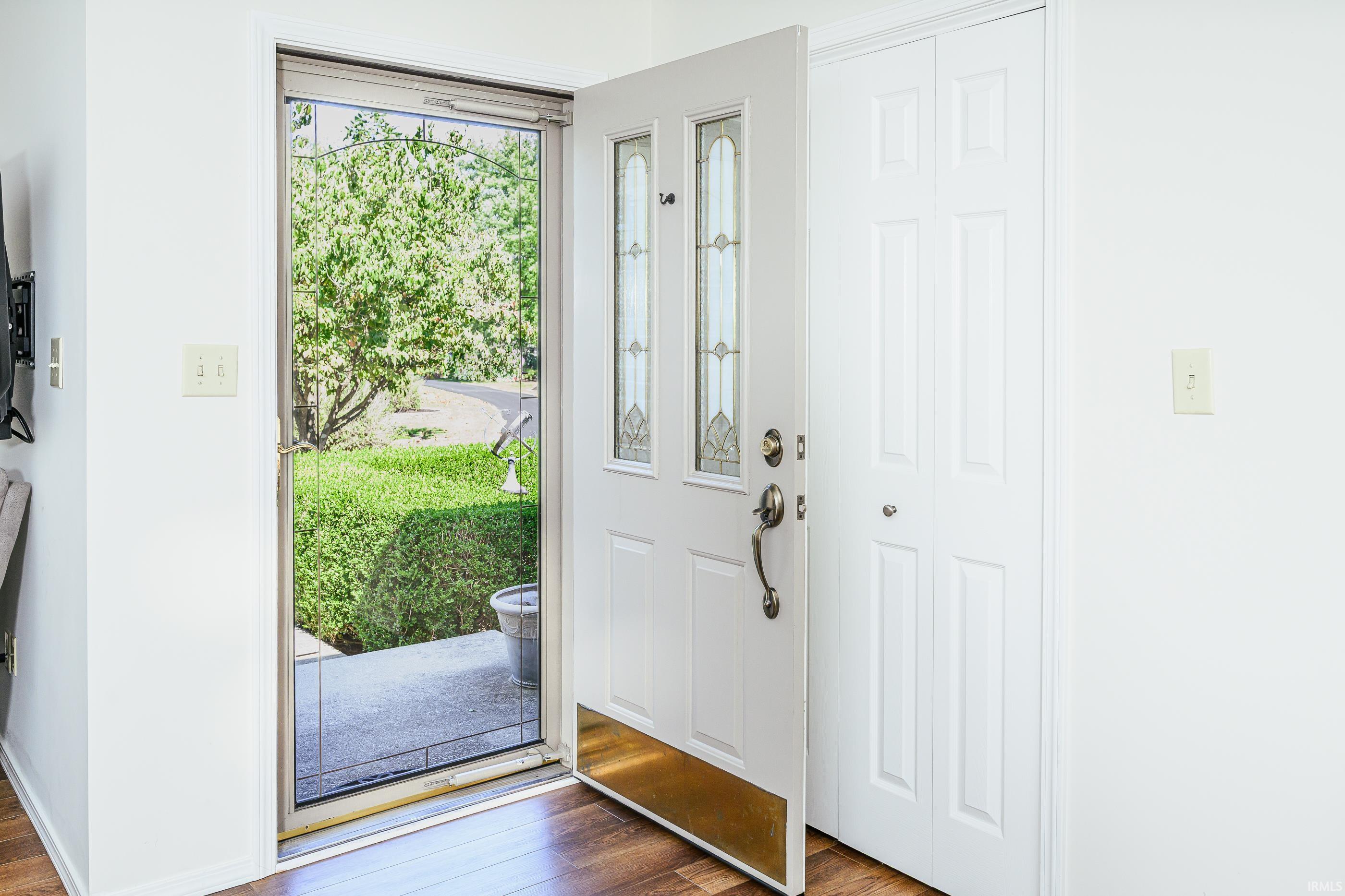 Entryway with an open decorative-glass front door and a view of the hedge and walkway outside.