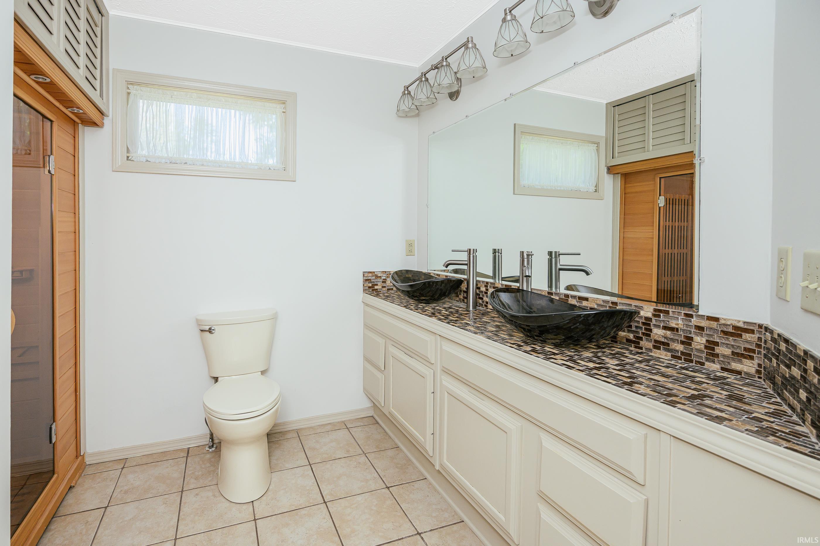Bathroom with double dark vessel sinks, a mosaic vanity backsplash, and a large mirror.
