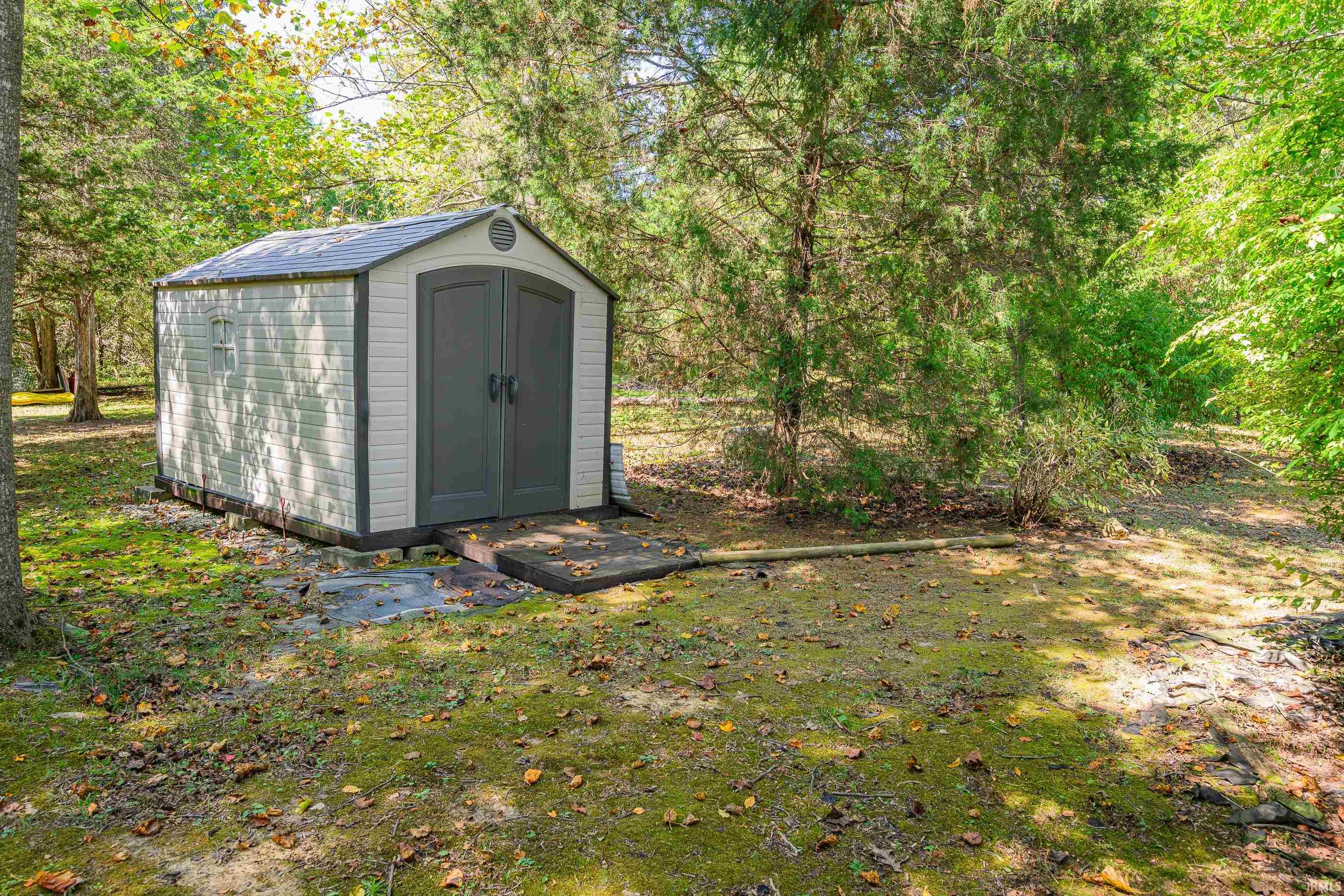Storage shed in a wooded yard, with dark double doors and a small entry platform.